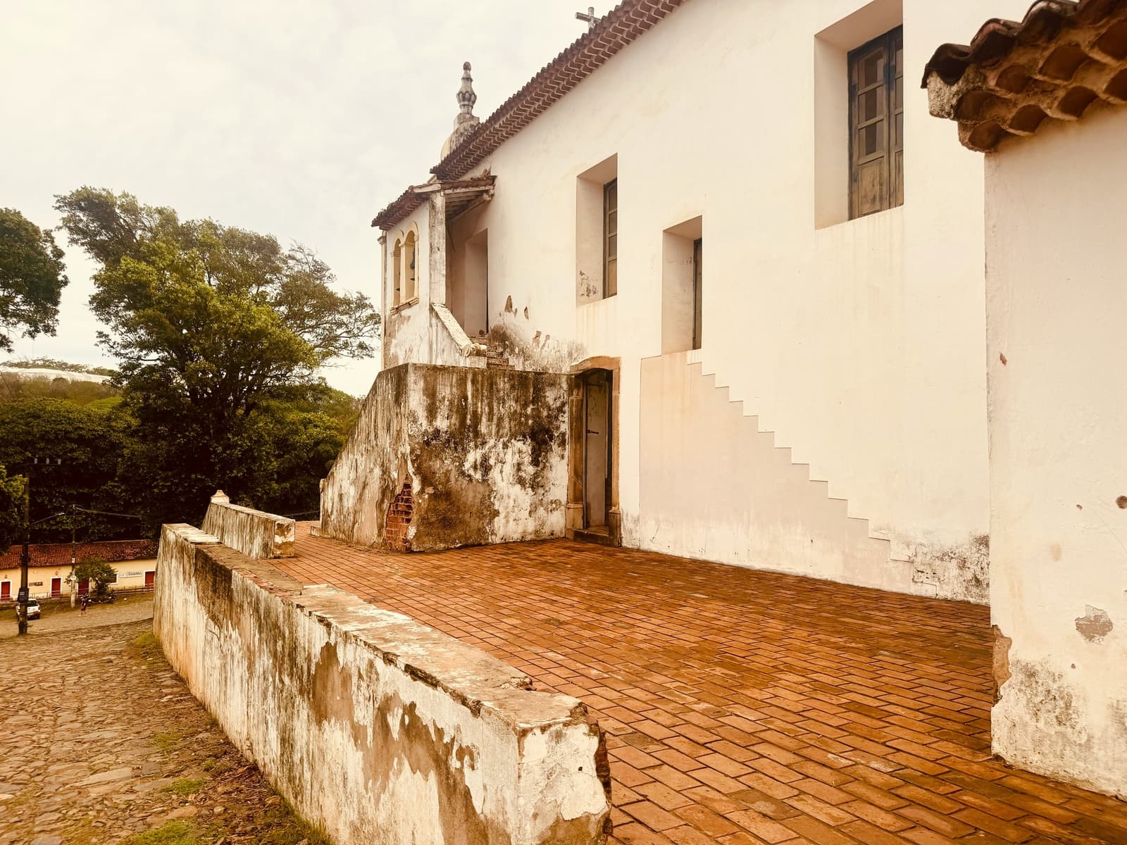 Eeuwen zeelucht hebben dit kapelletje zijn mooiste patina gegeven. Verweerde witte koloniale kerk met terracotta bakstenen terras en klokkentoren uitkijkend over een kinderkopjesplein in Fernando de Noronha