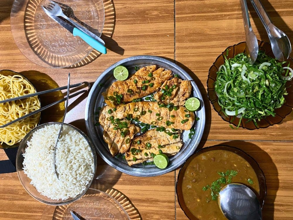 Du poisson bien épicé, du riz, des herbes fraîches, la cuisine du Maranhão ne fait pas semblant. Vue de dessus d'un repas maison sur une table en bois – filets de poisson grillés garnis de citron vert et de ciboule, riz blanc, salade d'herbes vertes, nouilles jaunes et bouillon de haricots épais