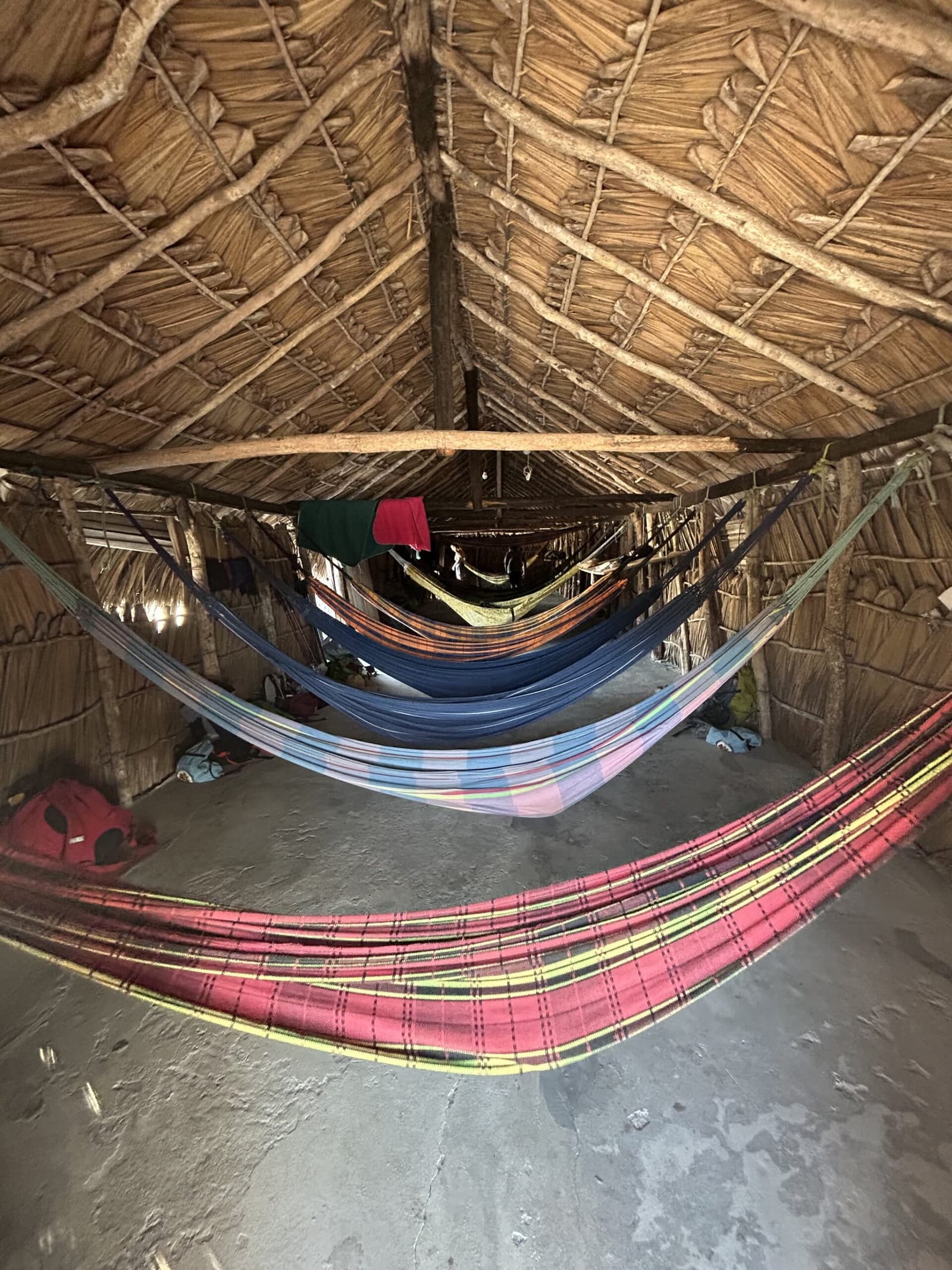 Le lit du soir, version locale. On s'y fait très vite. Hamacs colorés suspendus dans un abri rustique au toit de chaume lors du circuit à cheval dans les Lençóis Maranhenses, avec des sacs de voyage posés sur le sol en terre
