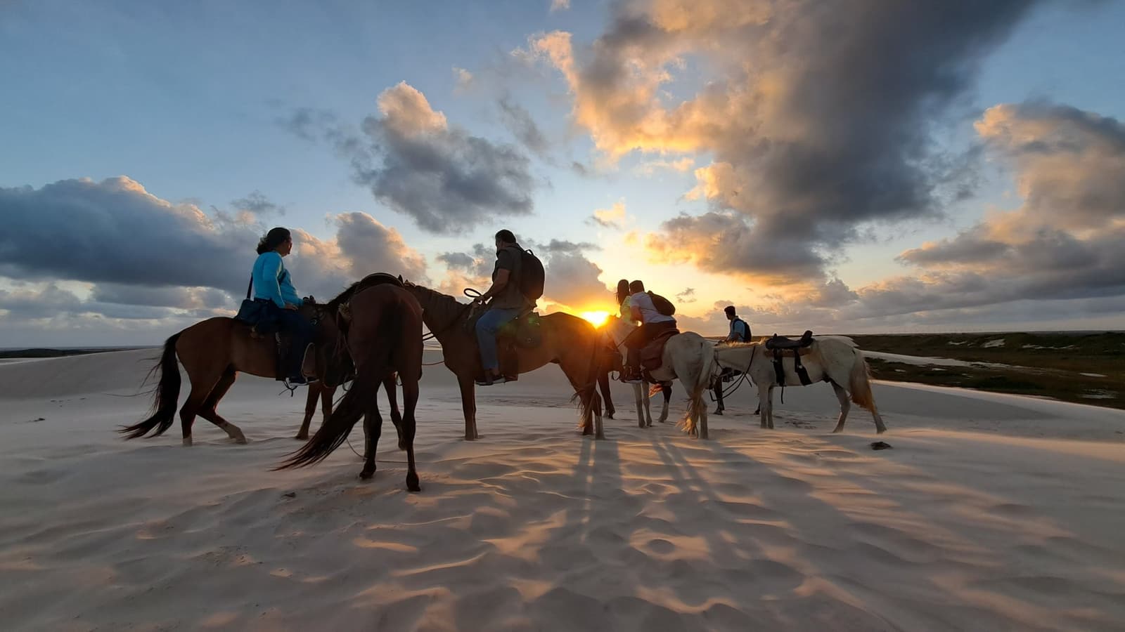 À cheval sur les dunes, quand le soleil décide de faire son cinéma. Un groupe de cavaliers en silhouette contre un coucher de soleil flamboyant sur les dunes de sable blanc des Lençóis Maranhenses, sous un ciel aux nuages dramatiques