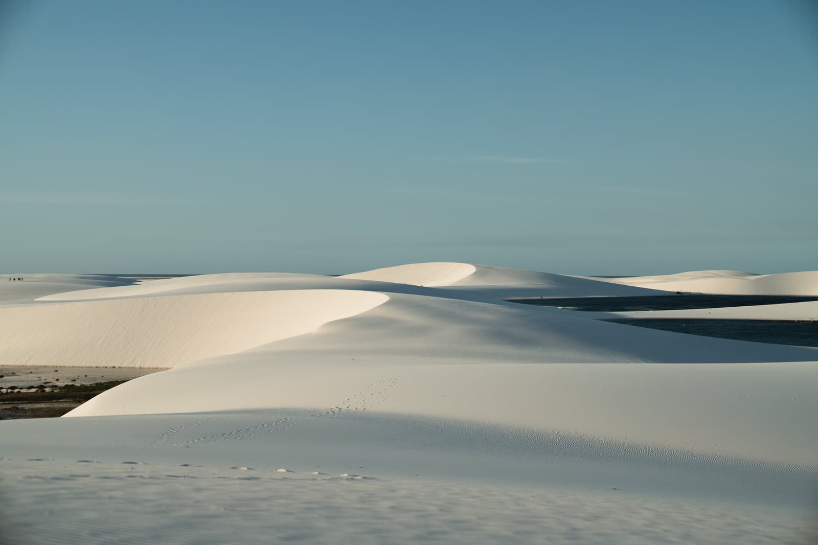 Du sable blanc à perte de vue, quelques lagunes, et des empreintes qui vous précèdent. Immenses dunes de sable blanc des Lençóis Maranhenses s'étendant jusqu'à l'horizon sous un ciel bleu limpide, avec des lagunes peu profondes visibles entre les crêtes ondulées
