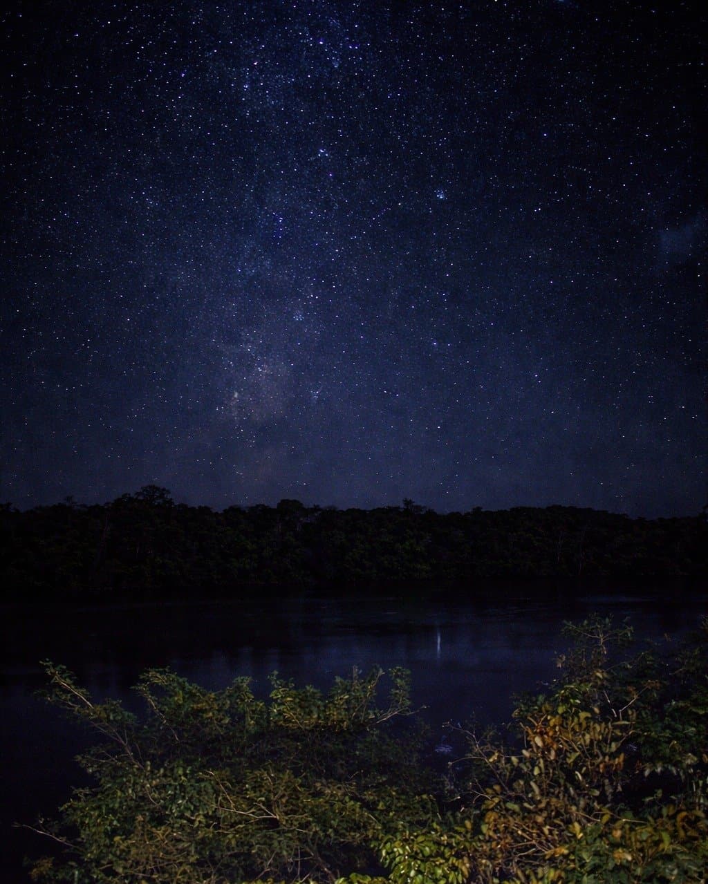 Longe o suficiente da cidade para lembrar quantas estrelas existem. A Via Láctea se estende por um céu estrelado sobre um rio escuro na floresta no Juma Amazon Jungle Lodge, com o núcleo galáctico refletido suavemente na água parada abaixo