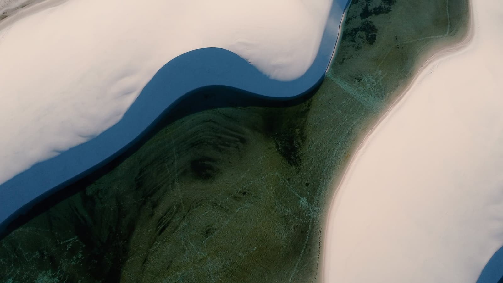 Sable, eau et profondeur — une toile abstraite invisible depuis le sol. Vue aérienne d'un lagon bleu profond serpentant entre des dunes de sable blanc avec une végétation aquatique verte visible sur le circuit de randonnée des Lençóis Maranhenses