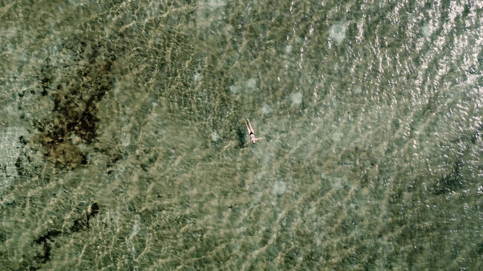 Seul au milieu d'une lagune transparente, suspendu entre ciel et sable. Vue aérienne d'un nageur solitaire flottant dans les eaux peu profondes et cristallines d'une lagune de la randonnée dans les Lençóis Maranhenses, le fond sableux visible sous la surface