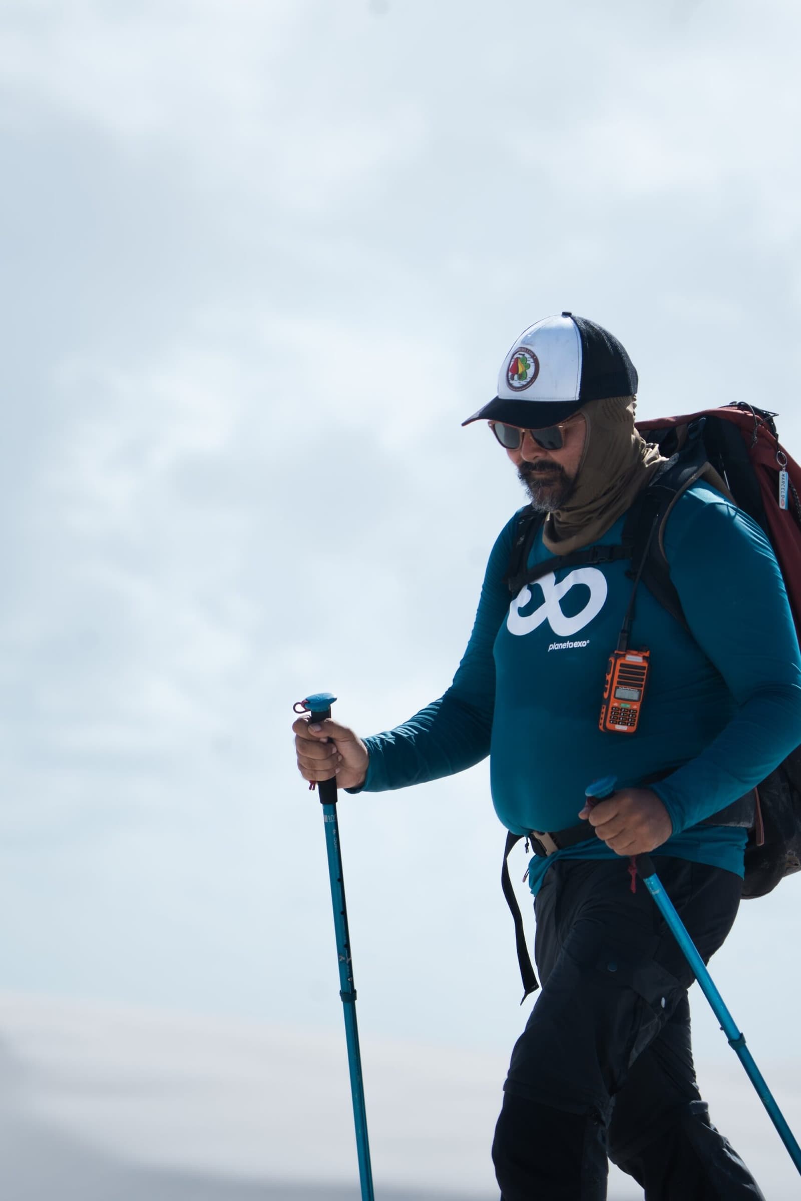 Bâtons en main, radio au baudrier, sac bien chargé — le guide ouvre la voie. Un guide PlanetaEXO équipé de bâtons de randonnée, d'un grand sac à dos et d'une radio dirige la randonnée dans les Lençóis Maranhenses sous un ciel nuageux
