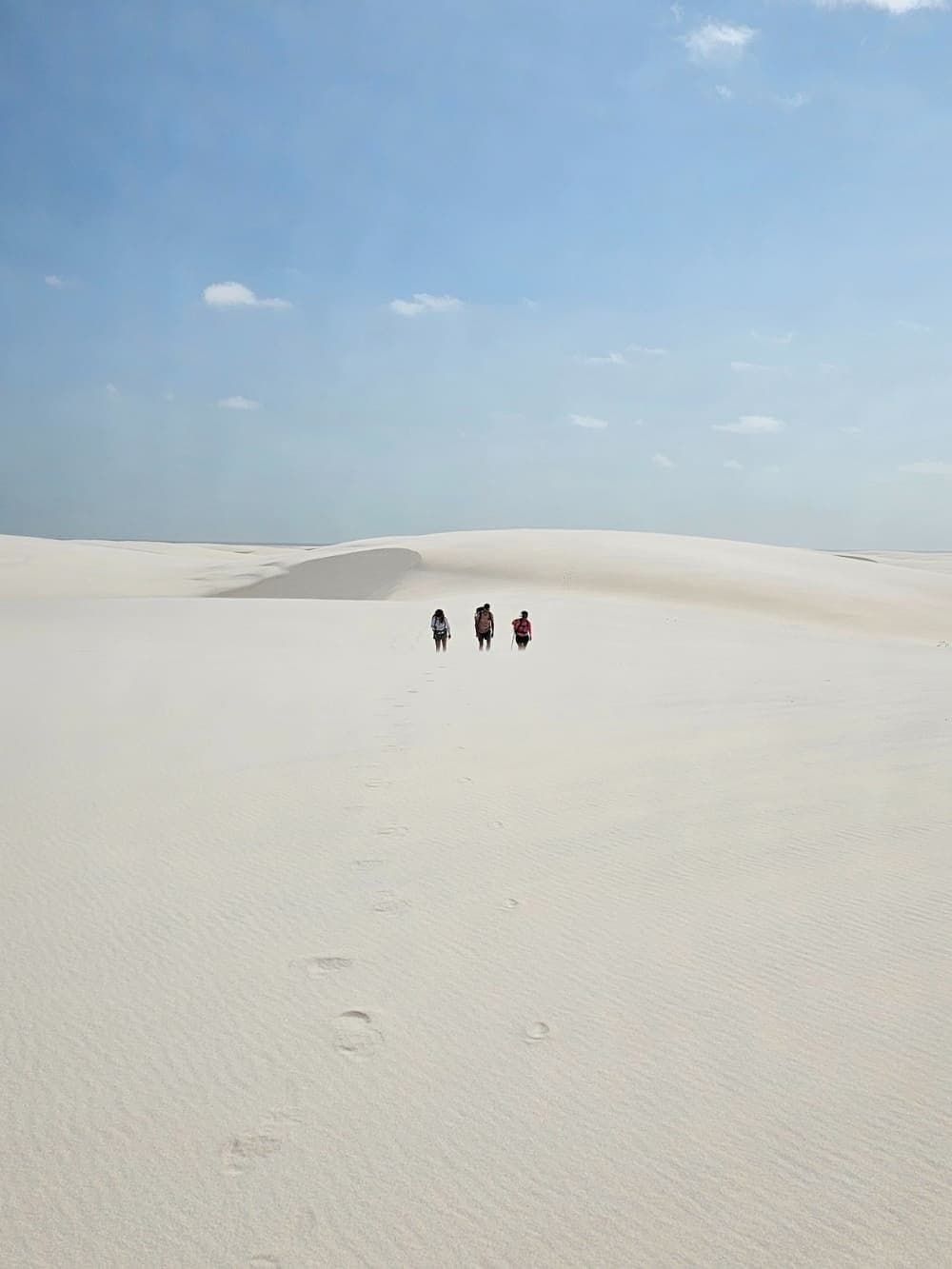 Trois silhouettes avalées par les dunes, leurs traces déjà à moitié effacées. Trois randonneurs progressent sur les immenses dunes de sable blanc lors d'une randonnée dans les Lençóis Maranhenses, leurs empreintes dessinant un chemin derrière eux