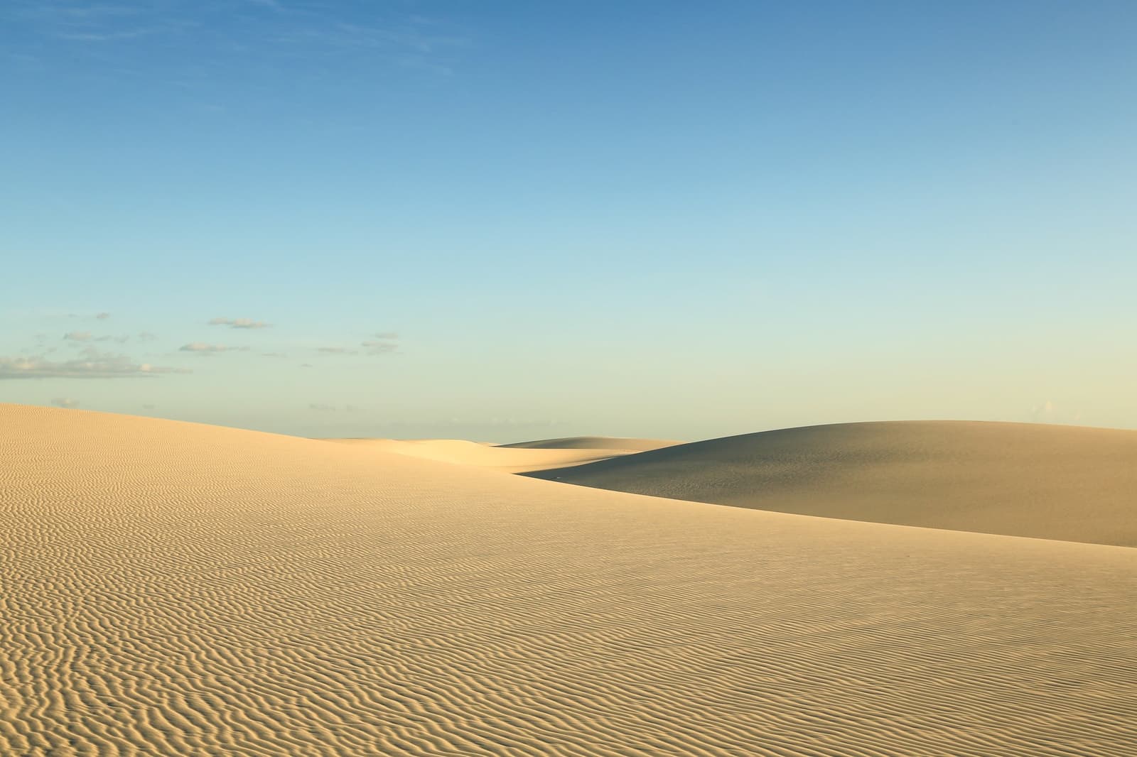 Crêtes sculptées par le vent, silence absolu — les dunes à l'état pur. Photo: Brunomsbarreto Vastes dunes de sable blanc sous un ciel bleu limpide sur le trek des Lençóis Maranhenses, avec des crêtes modelées par le vent jusqu'à l'horizon