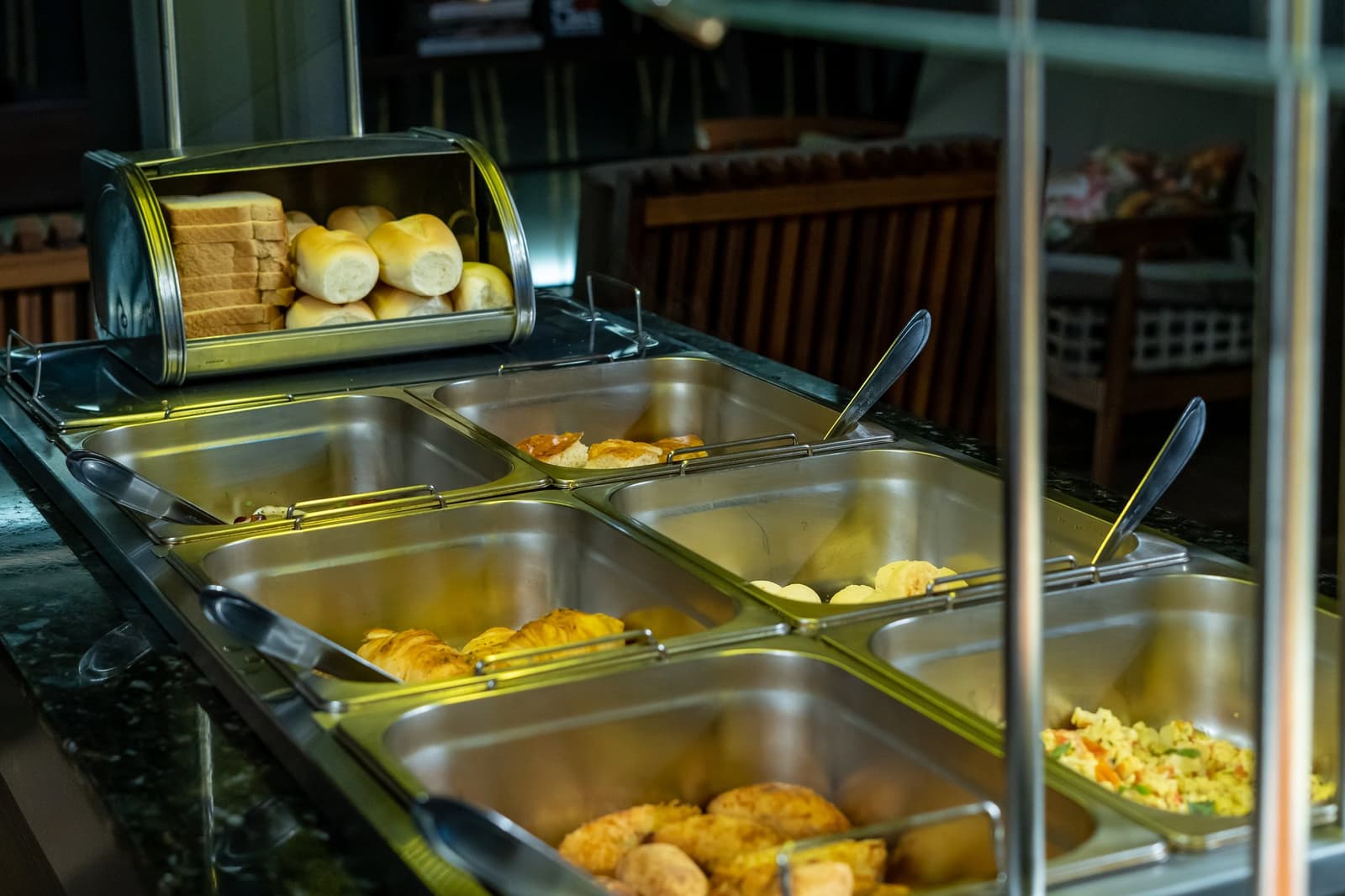 Fuel up before the river does the talking. A warm breakfast buffet spread aboard a luxury Amazon cruise in Brazil, featuring golden pastries, bread rolls, sliced sandwich bread, scrambled eggs, and a vegetable rice dish in polished stainless-steel chafing trays