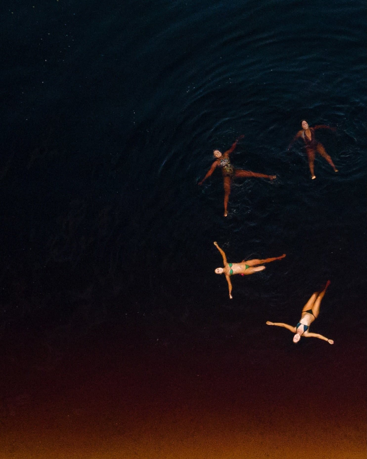 Four people, one dark river, and the sudden realization that this is the best idea of the trip. Aerial view of four swimmers floating on their backs in the dark tannin-rich waters of the Rio Negro, part of a luxury Amazon lodge Brazil experience