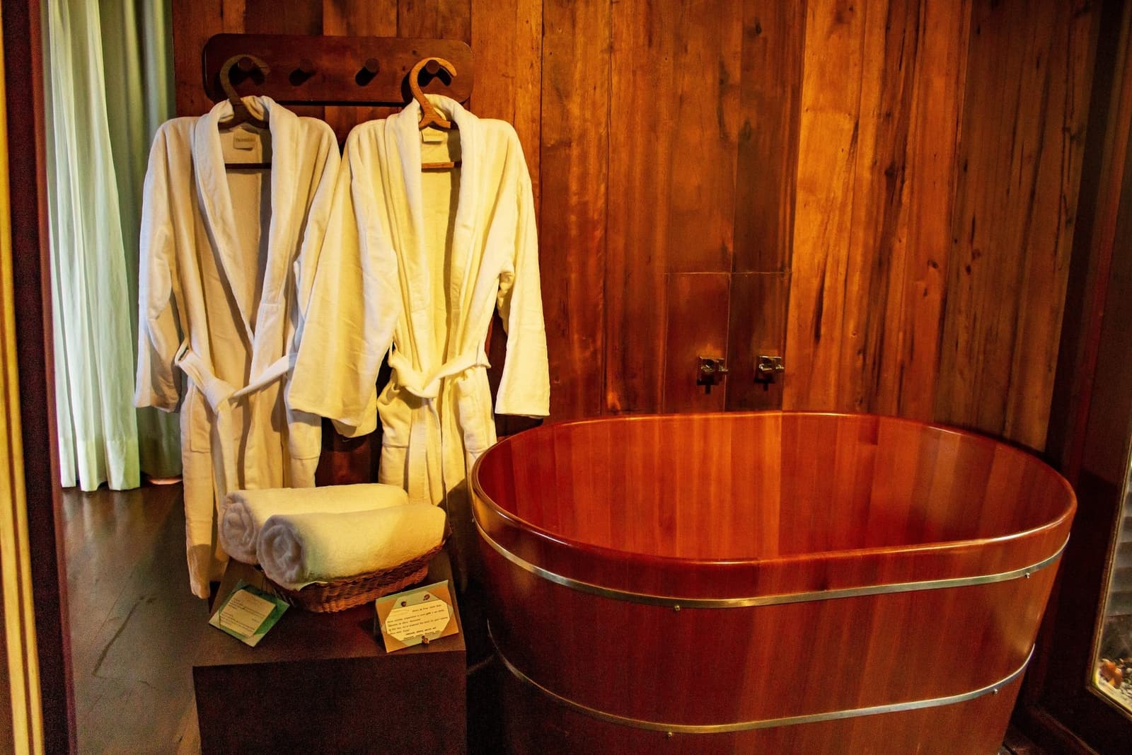 Your cue to slow down, the forest can wait a little longer. A polished round wooden soaking tub with brass fittings beside two white bathrobes hanging on a timber wall at a luxury Amazon lodge in Brazil