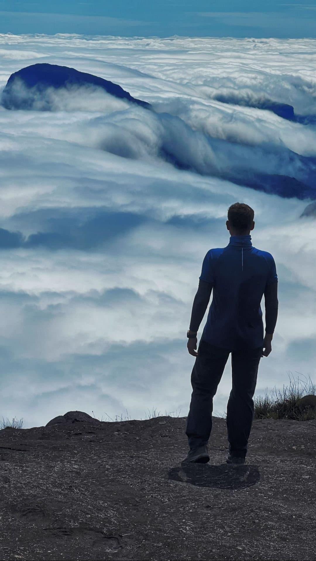 Les nuages en dessous, le silence au-dessus, le sommet change tout. Un randonneur se tient sur le plateau rocheux du sommet du Mount Roraima et contemple une vaste mer de nuages qui engloutit les tepuis environnants