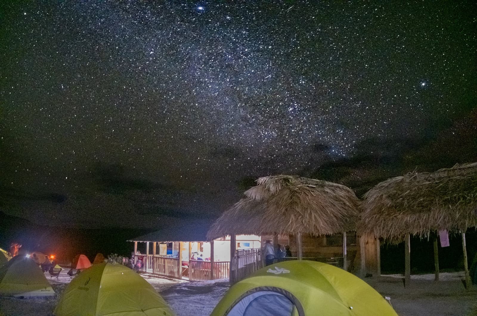 Un toit de paille, des toiles de tente, et la Voie lactée en guise de plafond. Tentes dôme vertes et abris au toit de chaume dans un campement isolé lors du trek du Mont Roraima, sous une Voie lactée éclatante