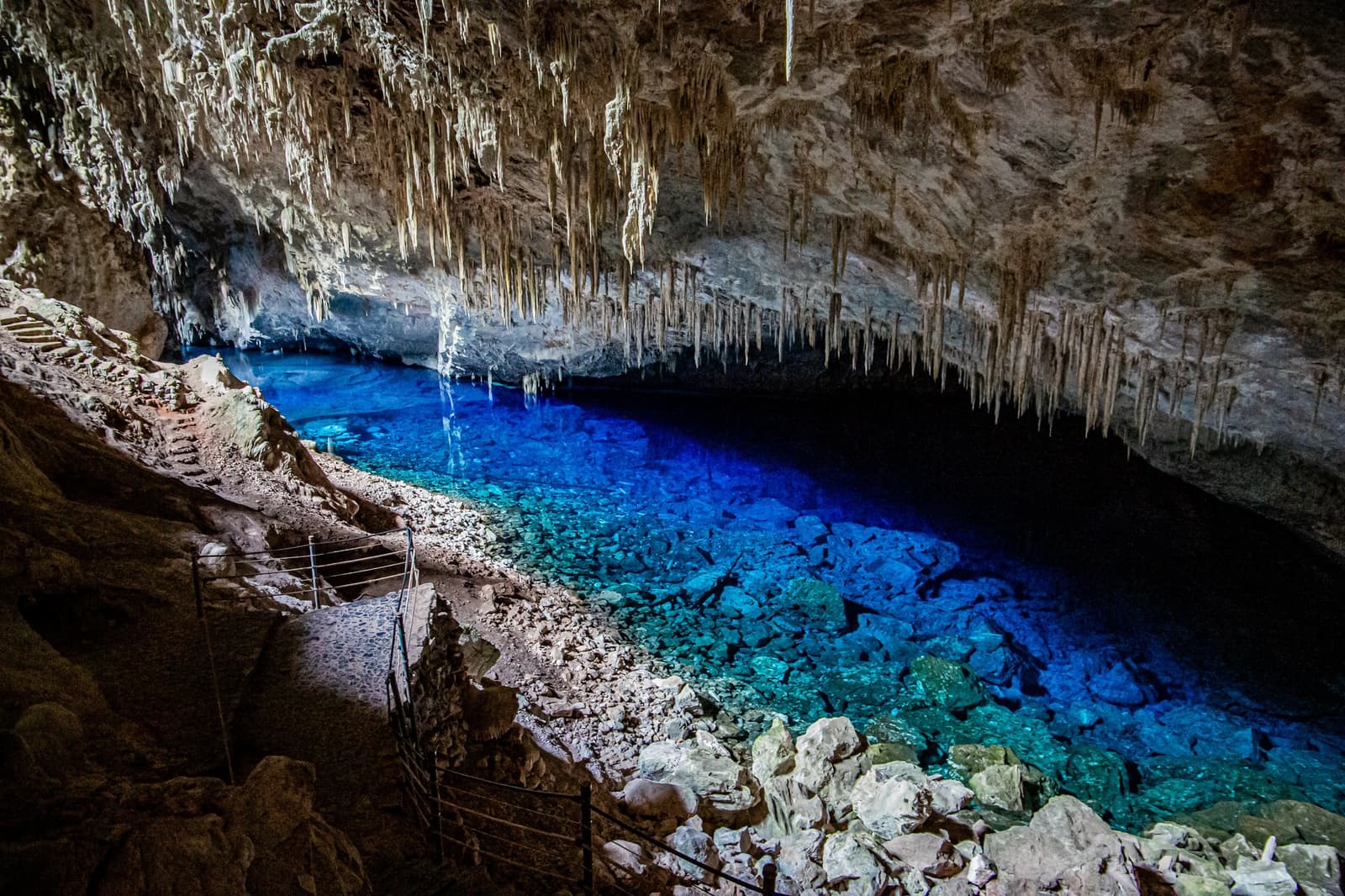 Die schönsten Blautöne in Bonito findet man unter der Erde. Ein leuchtend türkisfarbener Höhlensee in einer Kalksteinhöhle auf dem Pantanal-Bonito-Tour, mit dicht herabhängenden Stalaktiten von der Decke und einem schmalen Beobachtungspfad am Felsufer