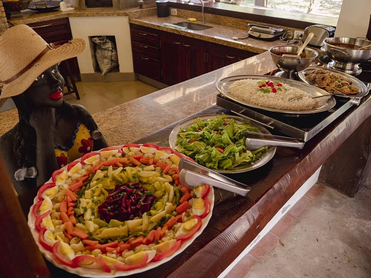 Im Pantanal wird auch am Mittagstisch gut für dich gesorgt. Buntes Lodge-Buffet auf einer Pantanal-Bonito-Tour mit einem dekorierten Salatteller mit hart gekochten Eiern, Karotten und Roten Beten sowie Reis, grünem Salat und panierten Gerichten auf einer Granittheke neben einer traditionellen Keramikfigur