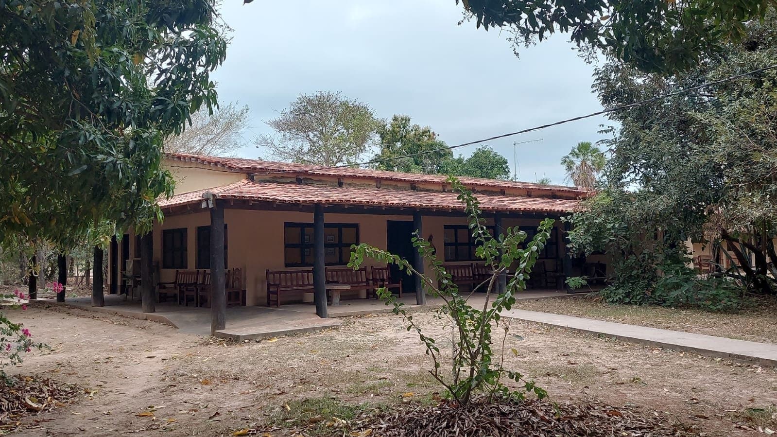 Sobre, ombragé, et franchement reposant après une journée de terrain. Lodge en adobe d'un étage avec toit en tuiles de terre cuite et véranda ombragée garnie de bancs en bois, entourée d'arbres matures dans le Pantanal