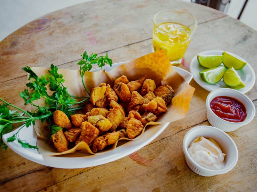 Petiscos crocantes e bem temperados para repor as energias entre os safáris. Um prato de petiscos fritos dourados com salsinha fresca, gomos de limão, ketchup e molho cremoso sobre mesa rústica de madeira