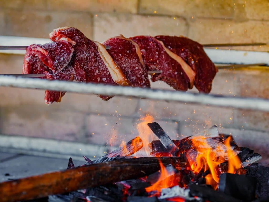 Brasa alta, sal grosso e carne vermelha, churrasco do sertão de verdade. Carne bovina com crosta de sal em espetos metálicos sendo assada sobre fogo de lenha aberto em uma pousada durante o safari de onças no Pantanal em Porto Jofre