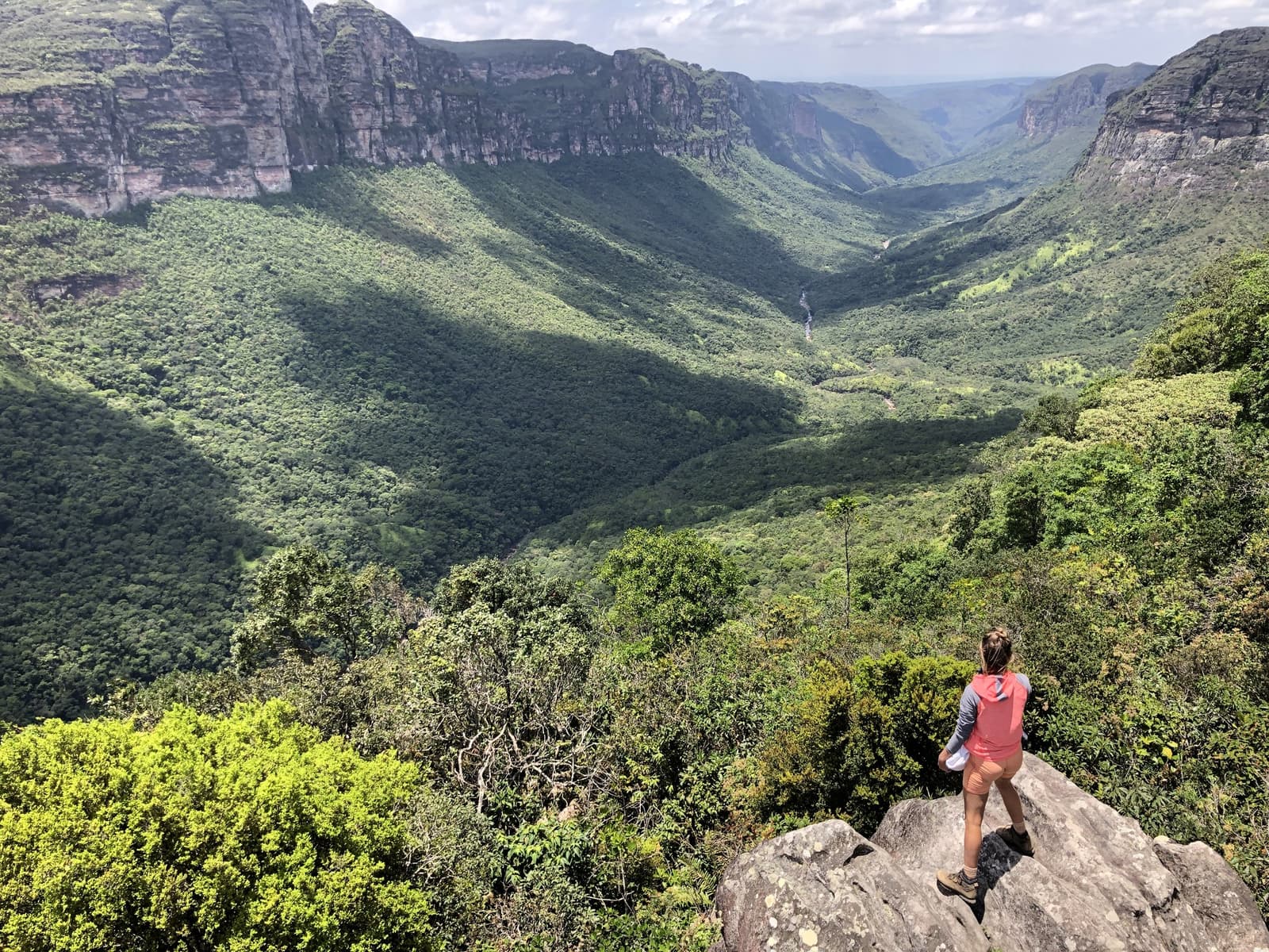 On pensait avoir atteint le bout du chemin, puis le canyon a dit non. Une randonneuse se tient sur un promontoire rocheux et contemple le vaste canyon boisé de la randonnée dans la Pati Valley, avec des falaises de grès et une cascade au loin