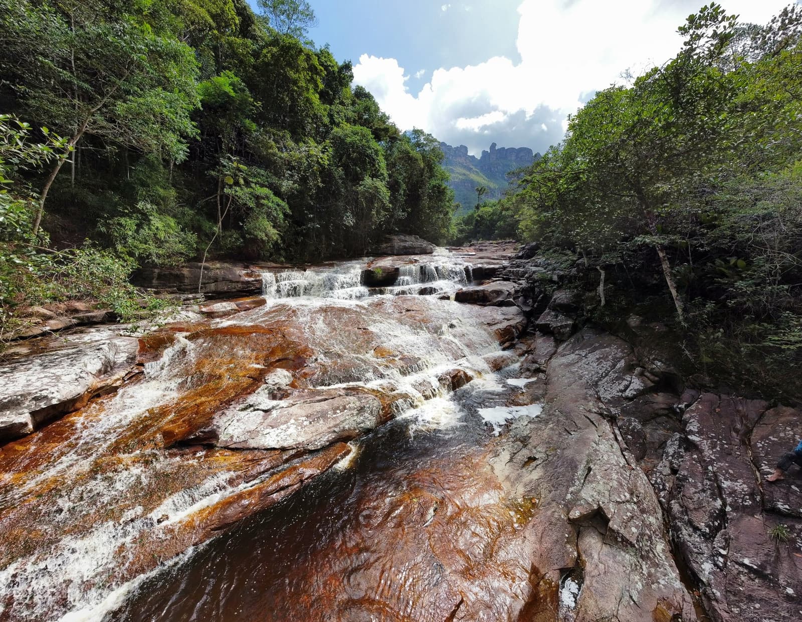 L'eau trace son chemin depuis des millénaires. Vous, vous avez l'après-midi. Eau claire dévalant des dalles de grès couleur rouille lors de la randonnée dans la vallée du Pati, forêt dense et sommets rocheux au loin sous un ciel nuageux