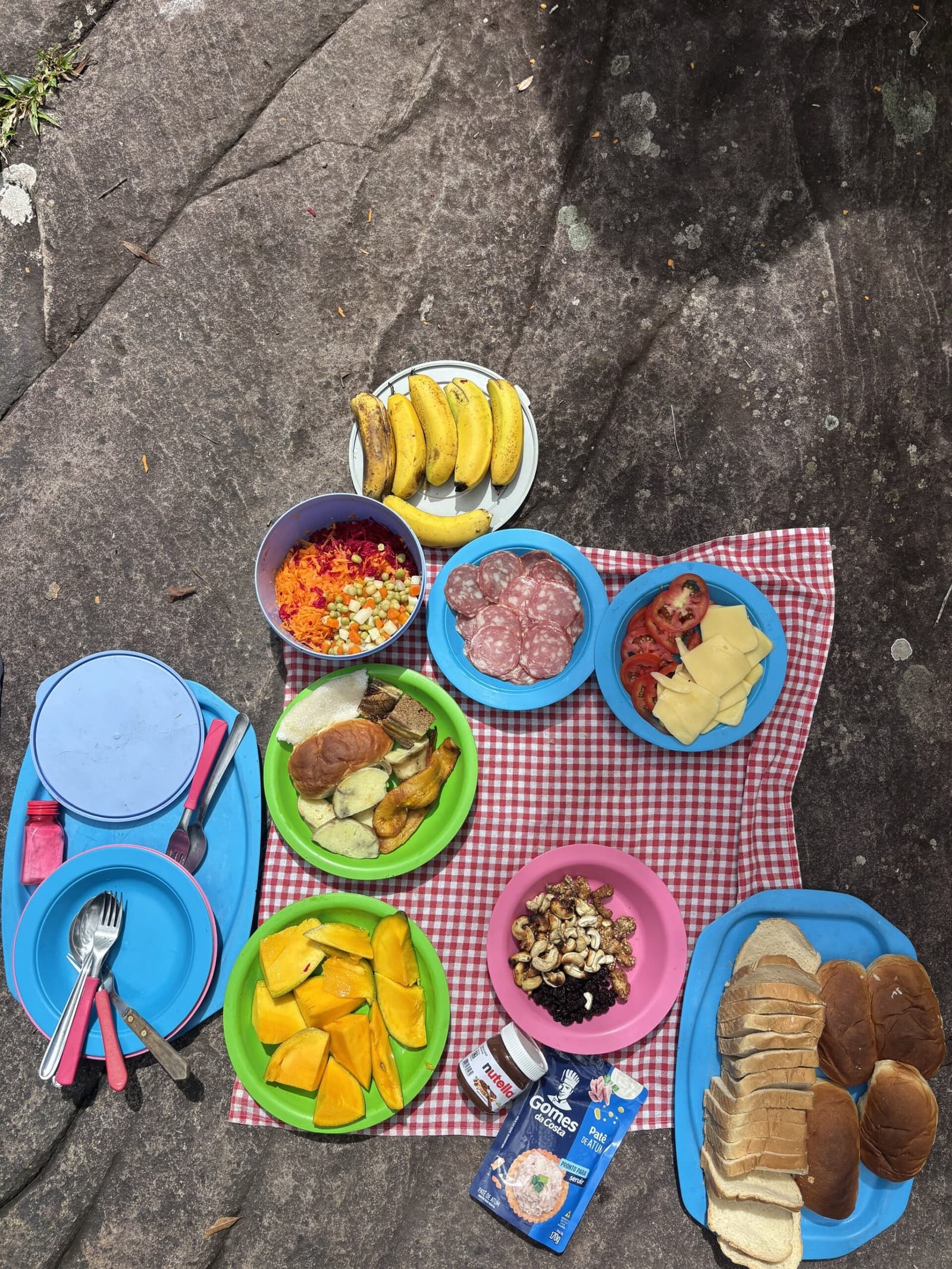 Un déjeuner sur le granit, sans menu ni serviette en tissu, et c'est très bien ainsi. Assiettes colorées de fruits, salami, fromage, légumes râpés, noix et pain tranché disposées sur une nappe à carreaux rouges et blancs posée sur un rocher lors d'un pique-nique sur le trek de la Pati Valley