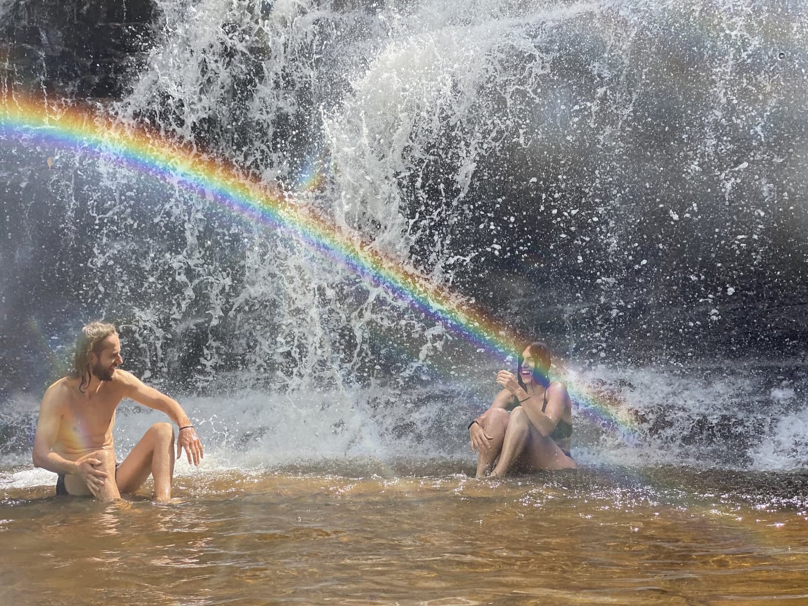 L'arc-en-ciel s'est invité tout seul, et personne n'a protesté. Deux voyageurs hilares assis dans le bassin peu profond d'une cascade lors de la randonnée dans la vallée de Pati, un arc-en-ciel vif traversant les embruns derrière eux