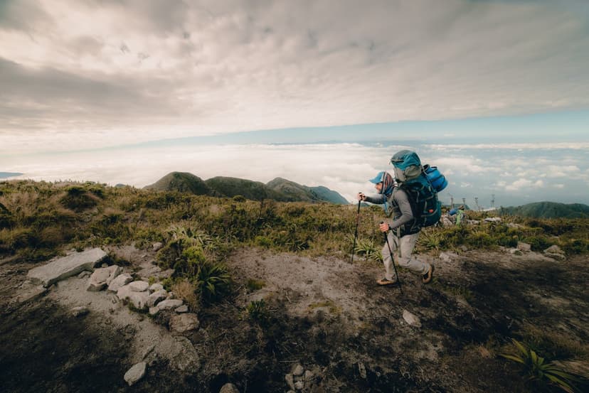 A hiker with a full backpack and trekking poles climbs a rocky high-altitude ridge on the Serra Fina Trekking route, with a sweeping sea of clouds and Mantiqueira peaks stretching to the horizon A hiker with a full backpack and trekking poles climbs a rocky high-altitude ridge on the Serra Fina Trekking route, with a sweeping sea of clouds and Mantiqueira peaks stretching to the horizon