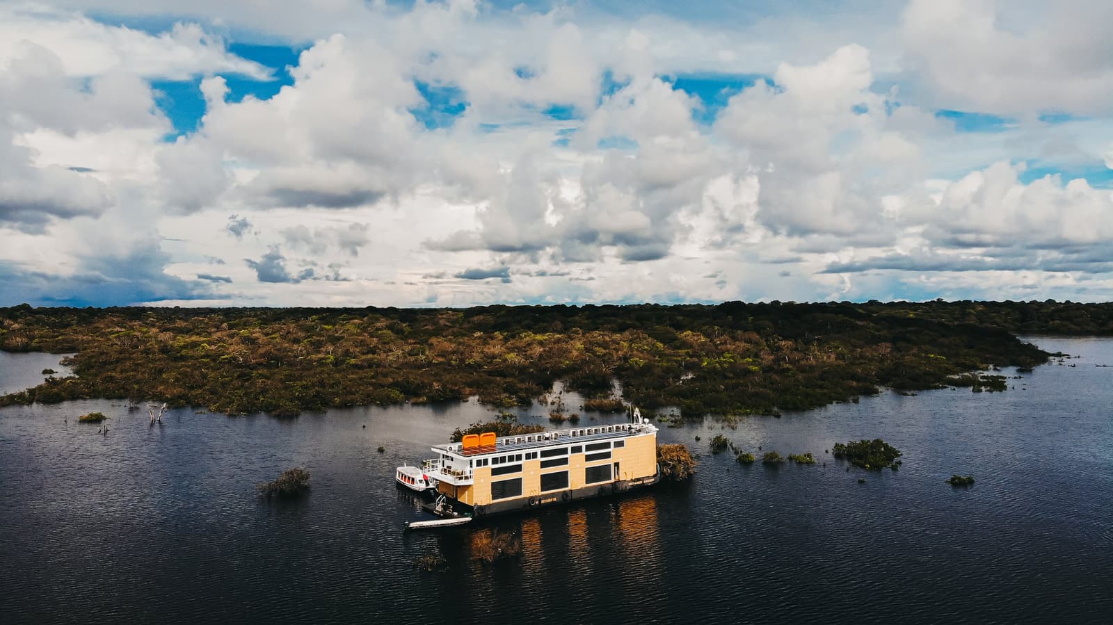 Un hôtel flottant posé au cœur de la forêt noyée. Vue aérienne du bateau de croisière Untamed Amazon amarré parmi des arbres inondés et des eaux sombres sous un ciel nuageux spectaculaire