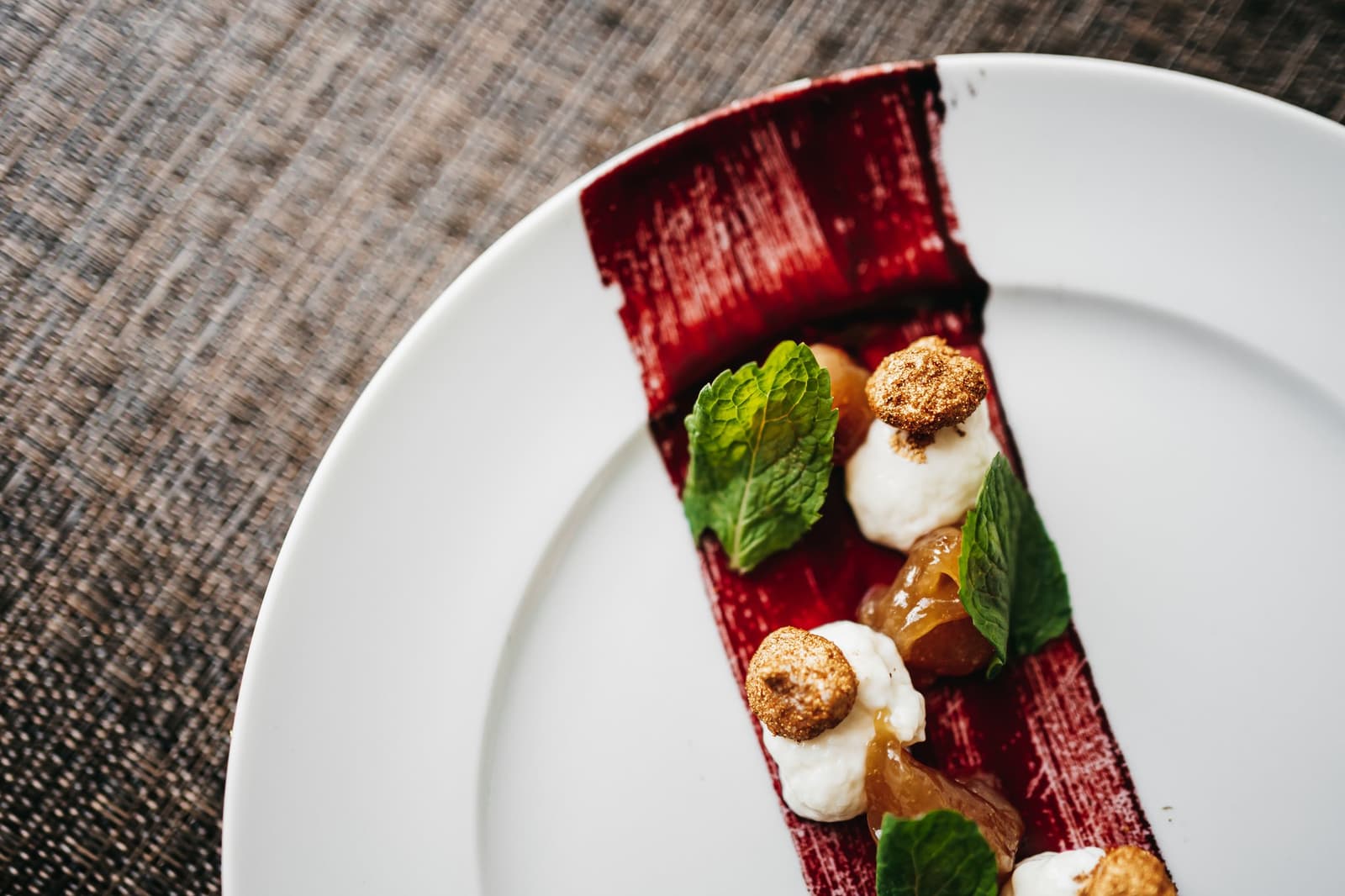 La jungle dehors, la finesse dans l'assiette, l'Amazonie sait surprendre à table. Dessert élégamment dressé sur une assiette blanche ronde : une base rectangulaire rouge profond surmontée de quenelles de crème, de miettes épicées, de gel de fruit translucide et de feuilles de menthe fraîche, servi à bord de l'Untamed Amazon Cruise