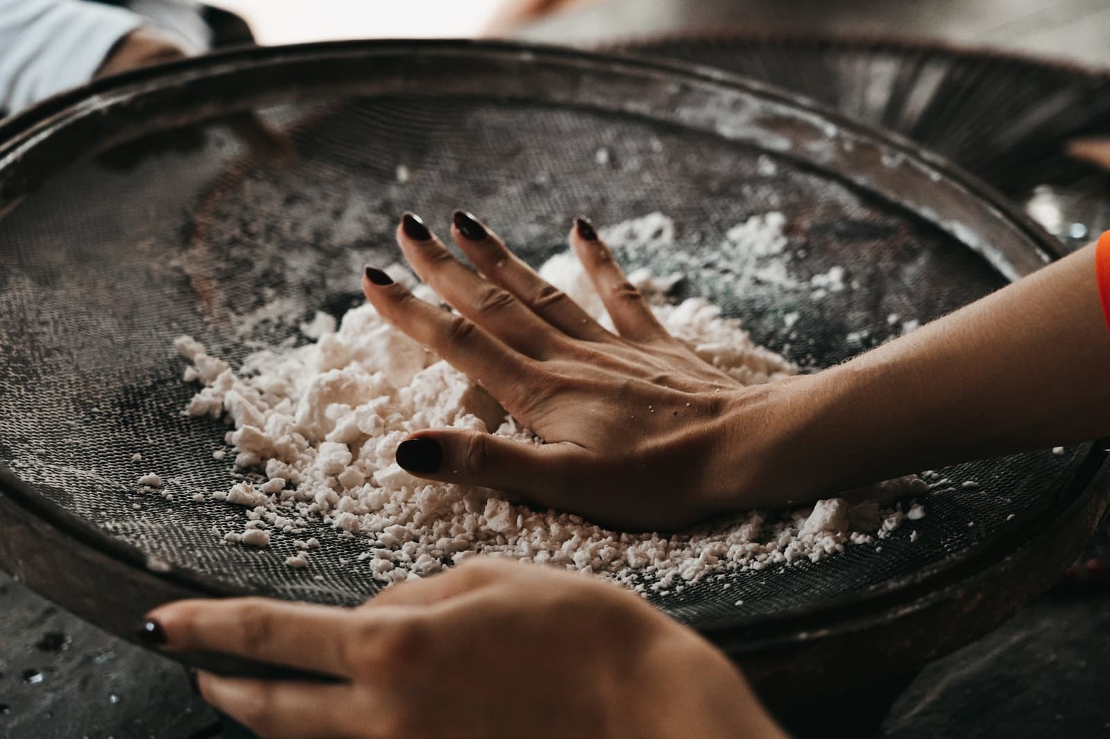 La farine de manioc, avant d'arriver dans votre assiette, passe par ces mains-là. Des mains pressent du manioc râpé à travers un grand tamis métallique lors d'une visite communautaire pendant la croisière Untamed Amazon