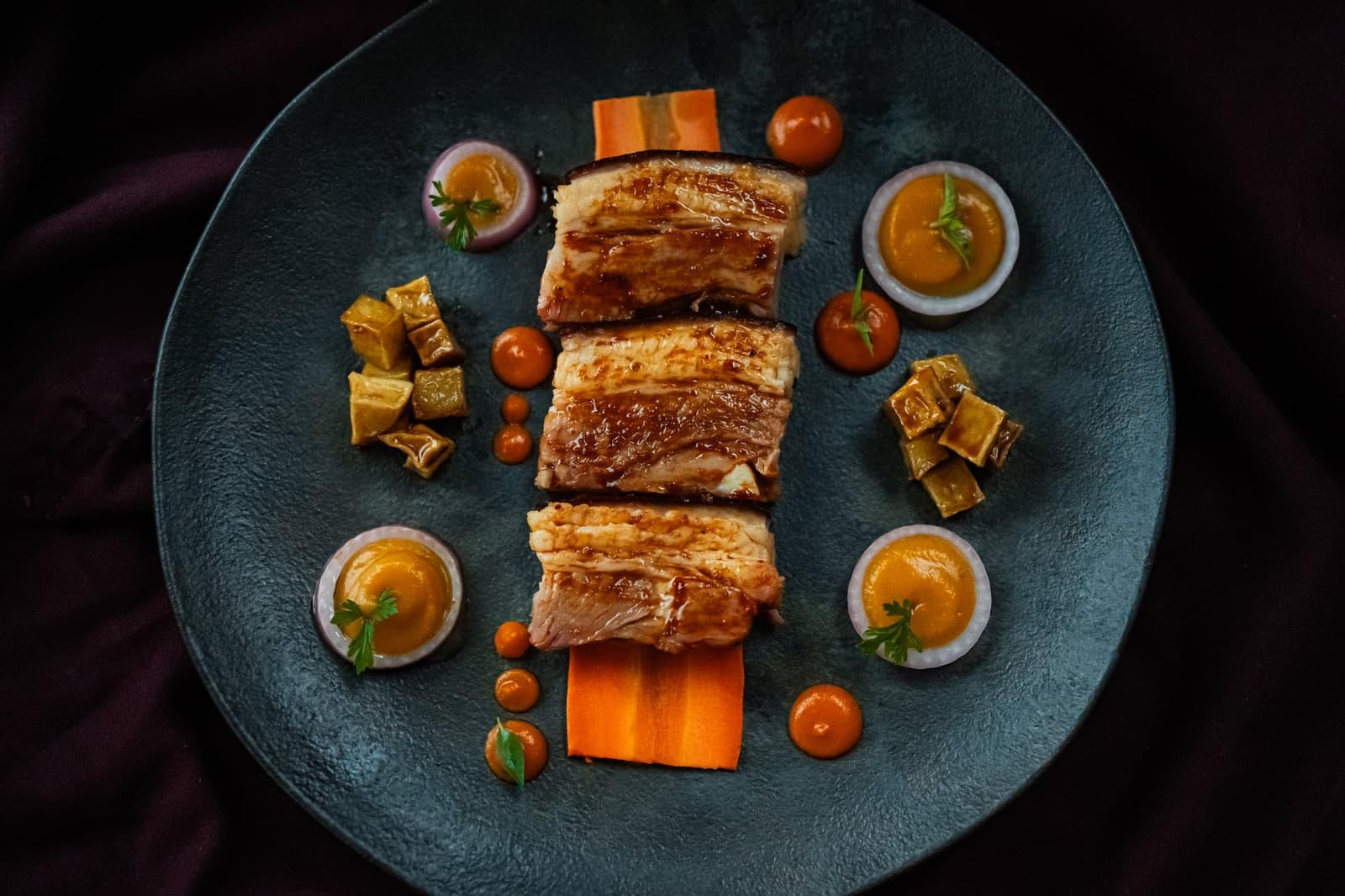 Sur le fleuve, la table aussi raconte quelque chose. Trois tranches de viande rôtie et glacée posées sur des rubans de carotte, entourées de coupelles de sauce dorée, de tomates cerises et de cubes de légumes braisés sur une assiette bleu-vert — gastronomie raffinée à bord de l'Untamed Amazon Cruise
