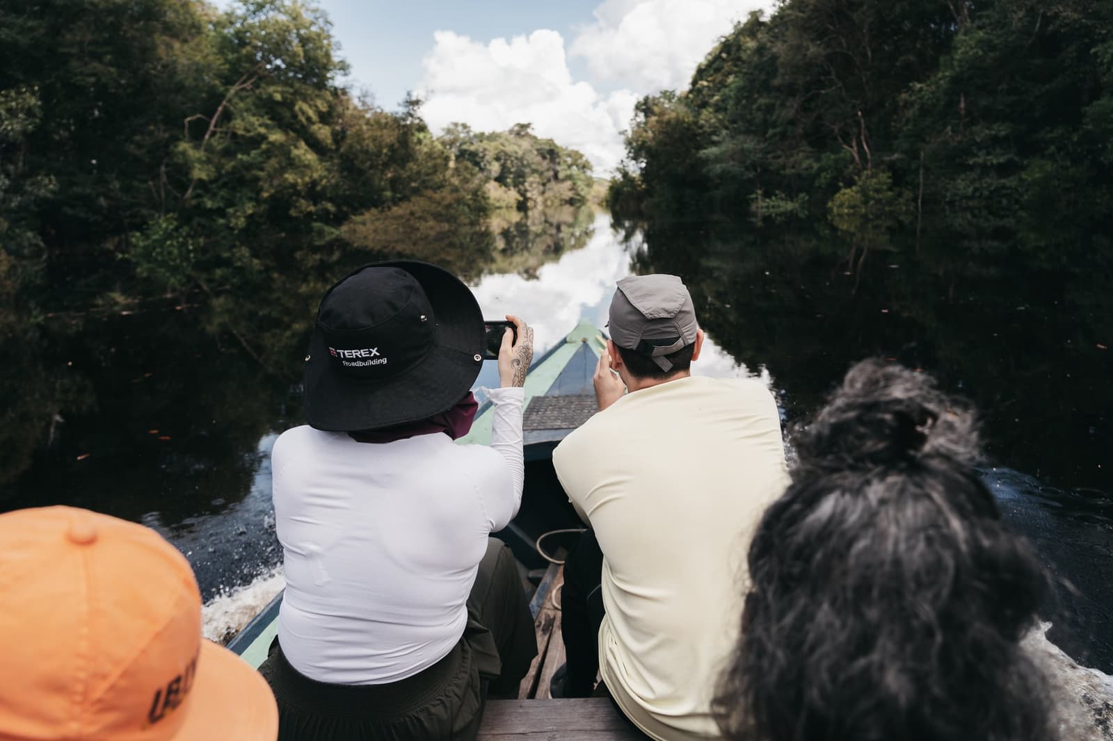 Sur ce fleuve, on range rarement l'appareil photo bien longtemps. Des écotouristes à bord d'un bateau en bois photographient un canal aux eaux miroitantes bordé d'une dense canopée amazonienne lors d'une croisière sur l'Amazone