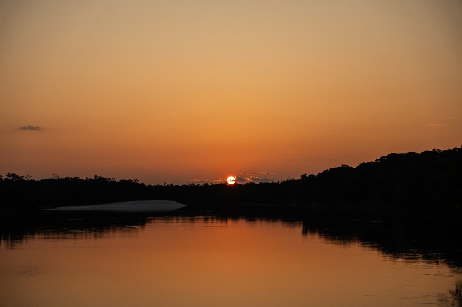 Le fleuve garde le ciel pour lui quand le soleil descend. Un soleil orange incandescent se couche derrière la silhouette sombre de la forêt tropicale, son reflet ondulant sur un fleuve calme avec un banc de sable blanc visible sur la rive gauche