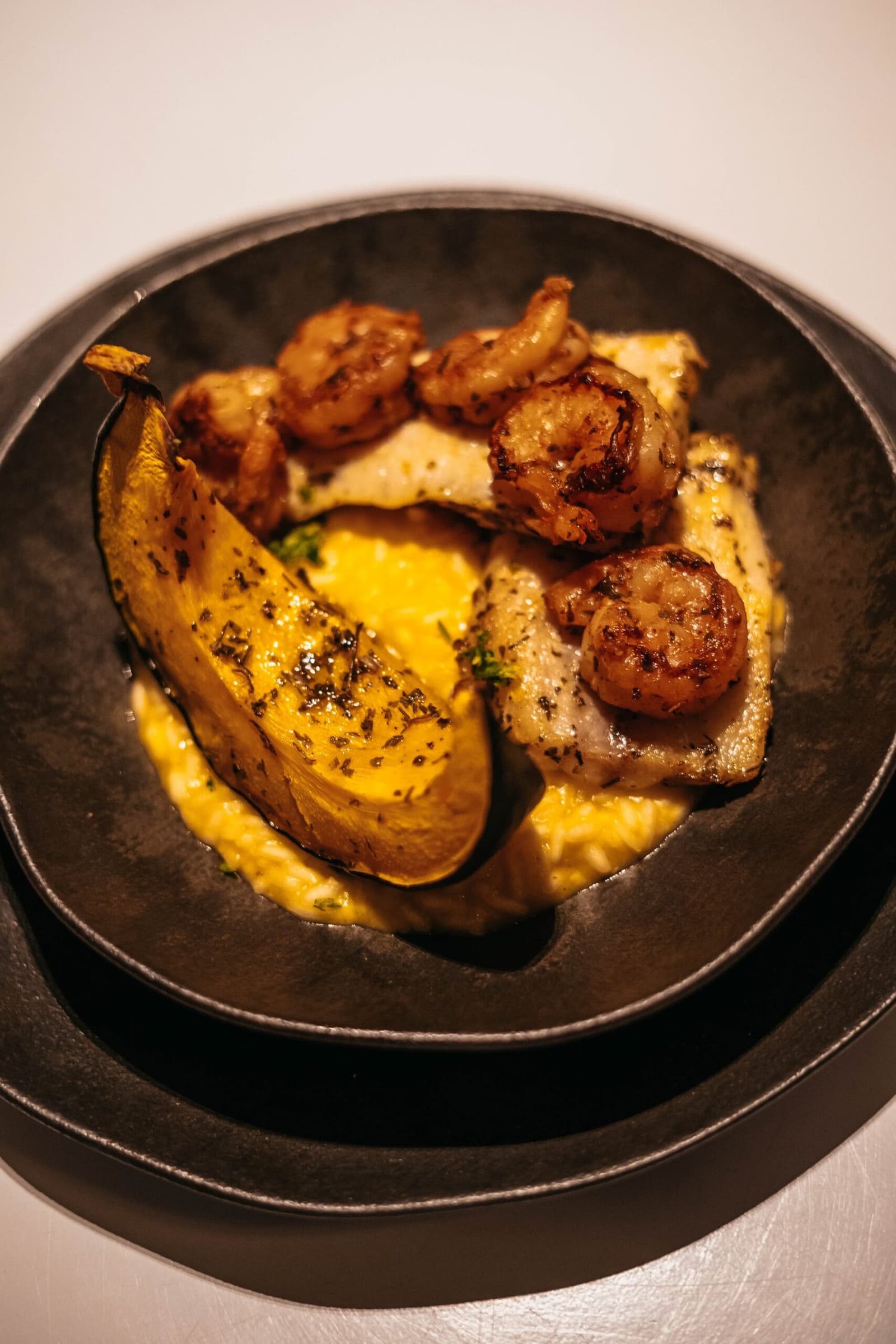 Poisson du fleuve, crevettes grillées, banane plantain, une assiette qui raconte le voyage. Crevettes poêlées et filet de poisson blanc dressés sur une sauce dorée crémeuse avec une demi-banane plantain carbonisée, dans un bol en céramique noire, à bord de l'untamed amazon cruise