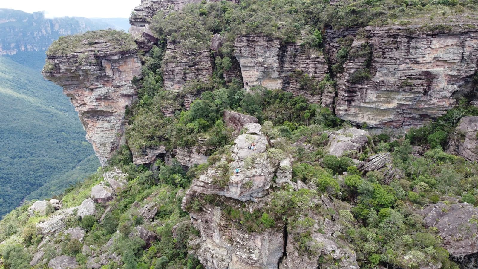 Des millions d'années de géologie, empilées et habillées de vert. Vue aérienne des falaises de grès stratifiées et de la végétation dense du Vale do Pati Trek, avec de minuscules randonneurs visibles sur un éperon rocheux