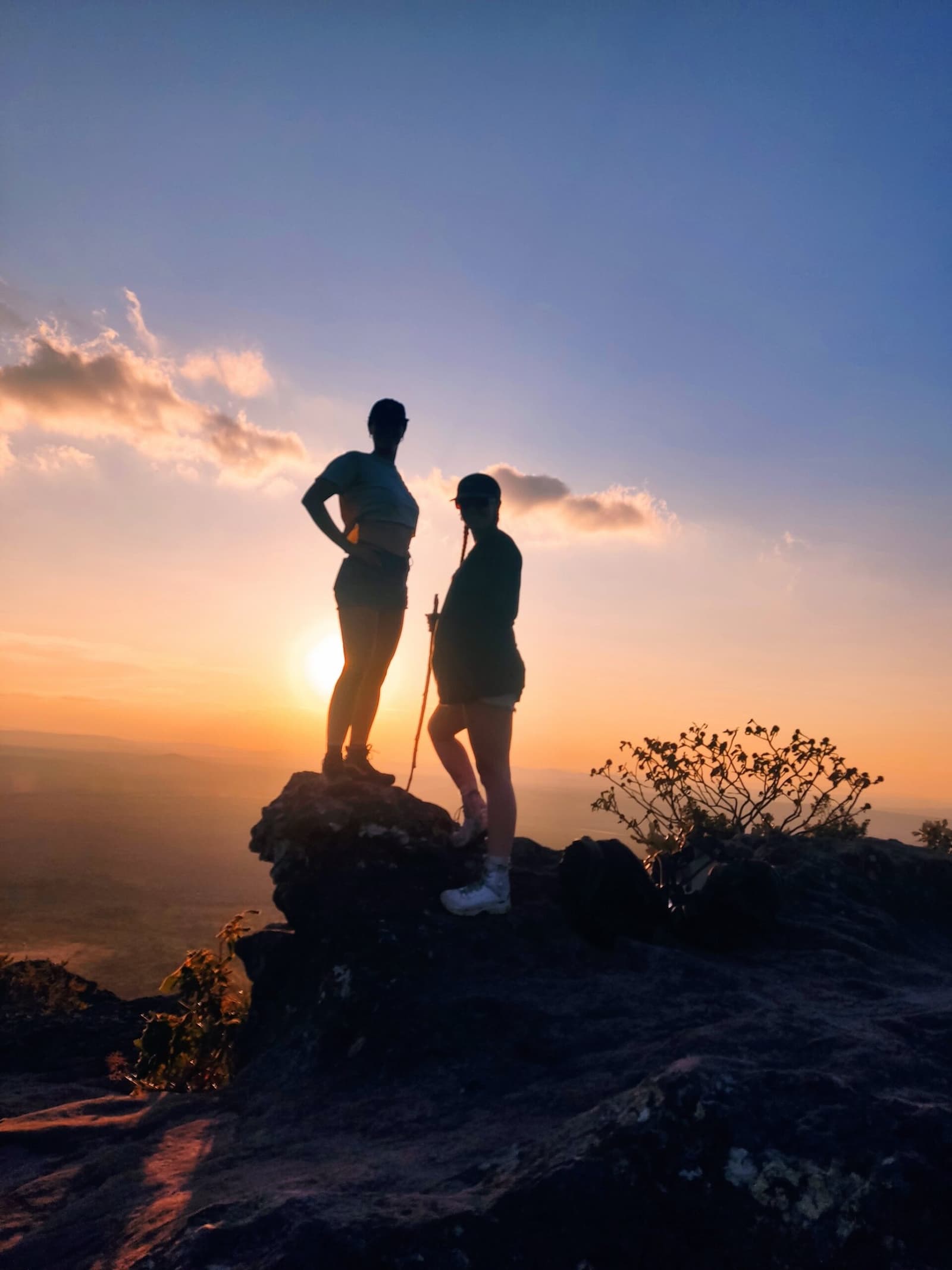 Le sommet se mérite, et ça, c'est la récompense. Deux randonneurs en silhouette au sommet d'un rocher lors du Vale do Pati Trek, face à un coucher de soleil orange embrasant une plaine immense