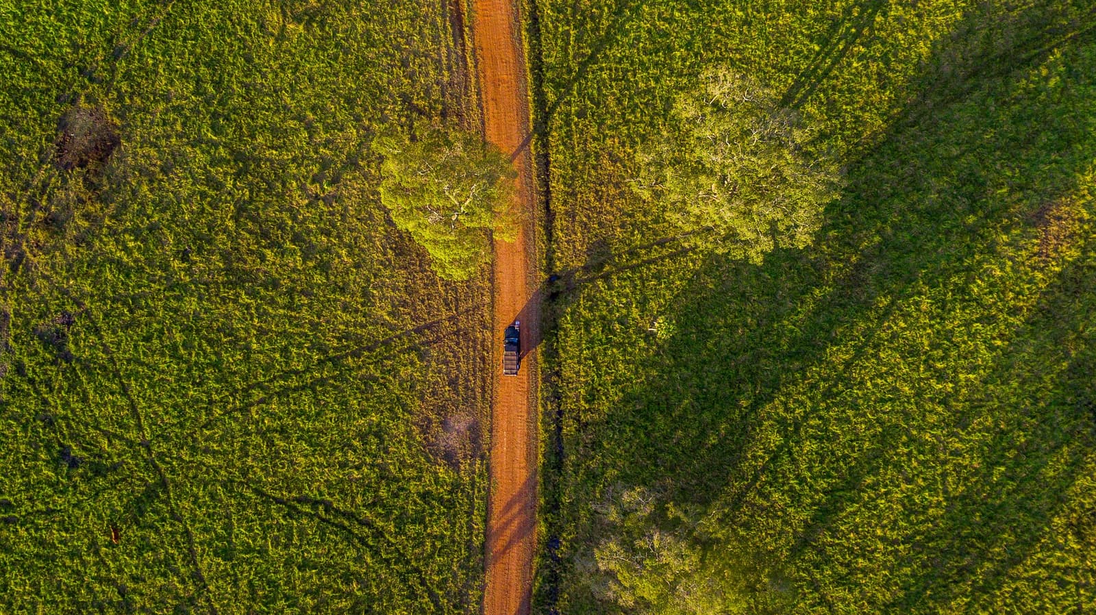 Dreiundfünfzigtausend Hektar, eine rote Piste, und du irgendwo mittendrin. Luftaufnahme von oben: Ein Fahrzeug auf einem roten Sandweg durchquert dichtes grünes Buschland auf einer Luxus-Pantanal-und-Amazonas-Reise