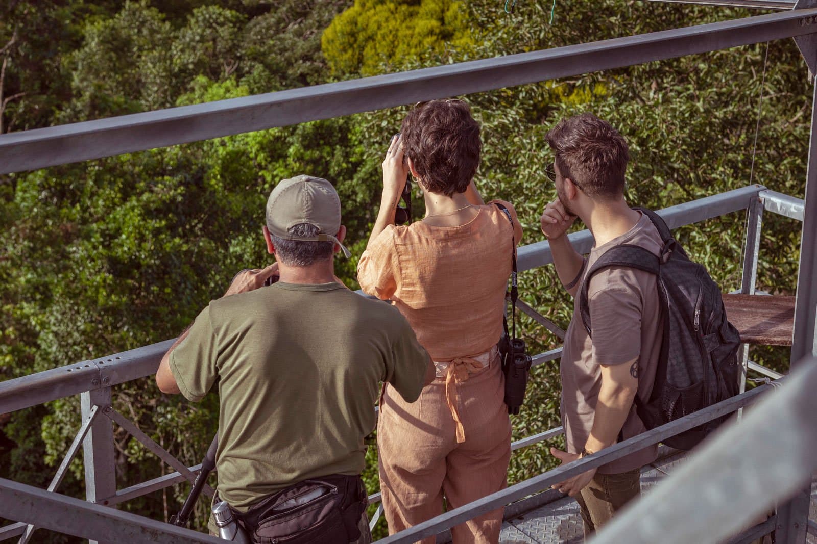 Ferngläser raus, Diskussion über die Vogelart beginnt in drei, zwei, eins. Photo: Samuel Melim Drei Besucher auf einem Metallturm über dem Baumkronendach beobachten mit Ferngläsern den Regenwald bei einer Luxus-Pantanal-und-Amazonas-Reise