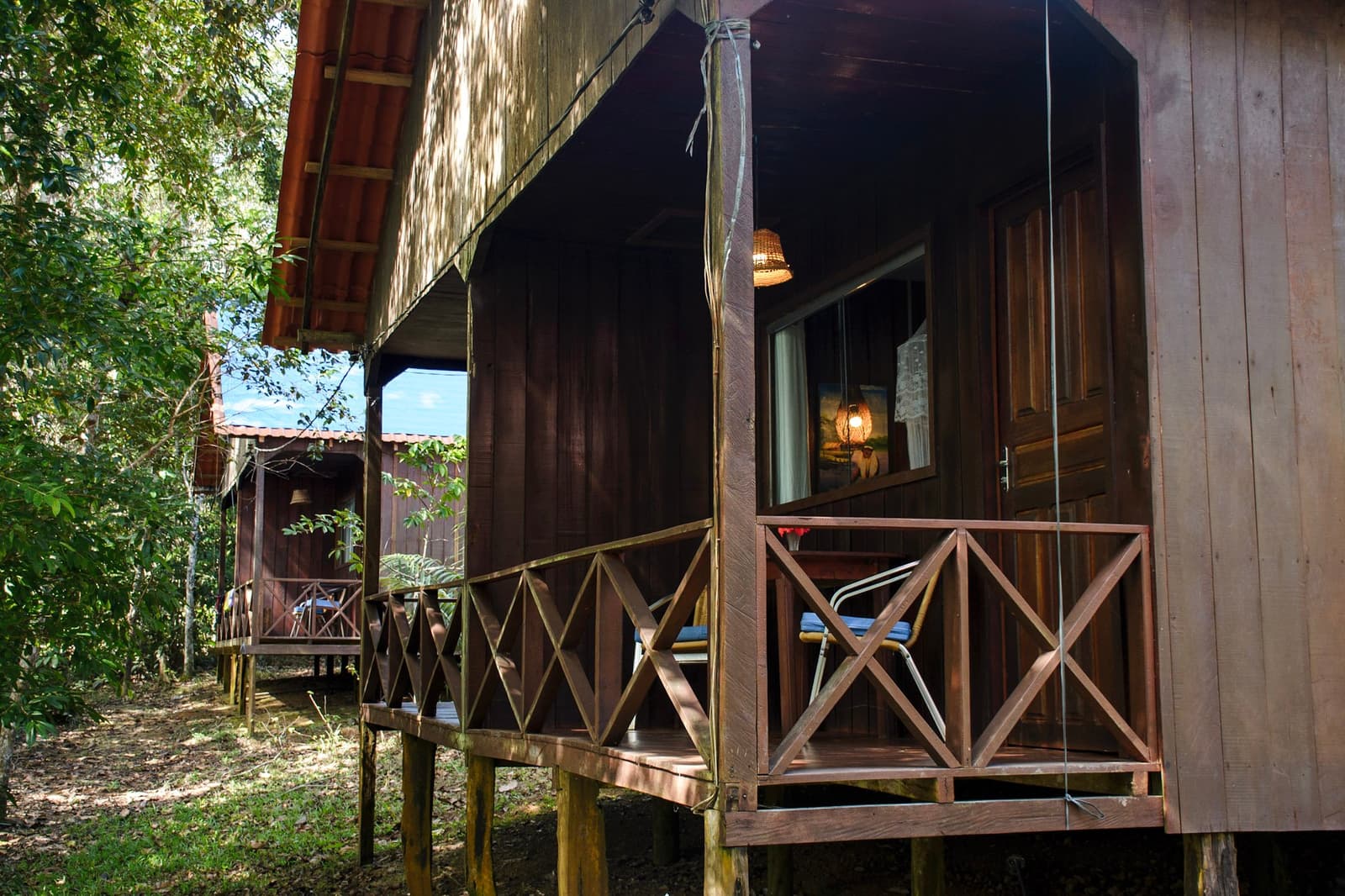 Hout, schaduw en een brandend lampje, genoeg comfort om morgen fris te beginnen. Twee verhoogde houten bungalows met kruislings gerailing veranda's, verscholen in schaduwrijk bos tijdens deze Amazon en Pantanal tour, met warm lamplicht zichtbaar door het raam van de dichtstbijzijnde hut