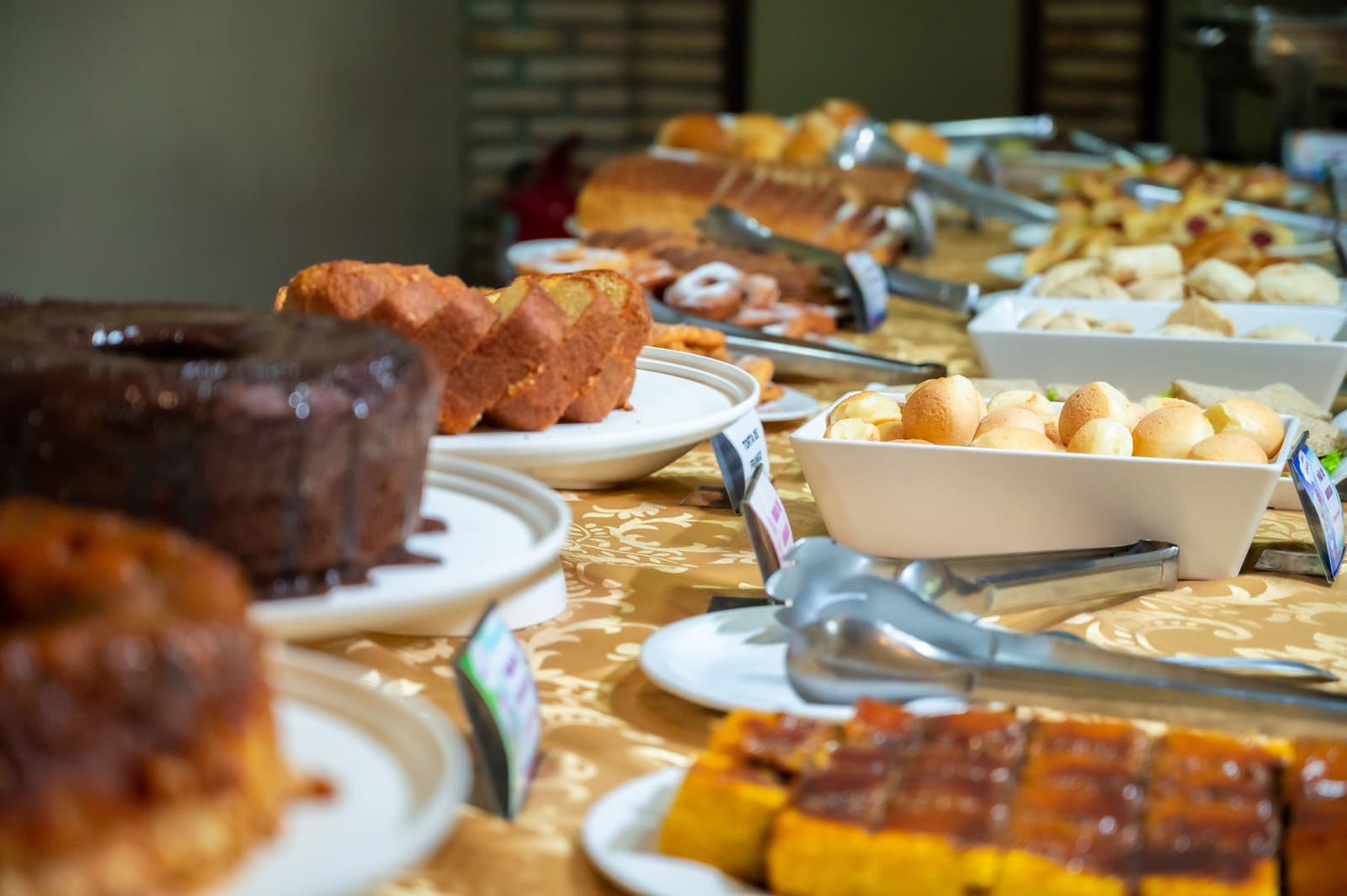 Goed ontbijten voor een dag jaguarspotten, zo doe je dat. Een uitgebreid ontbijtbuffet op een Amazon- en Pantanal-tour met gesneden cake, pão de queijo, zoete broodjes en gebak op een goudkleurig tafelkleed