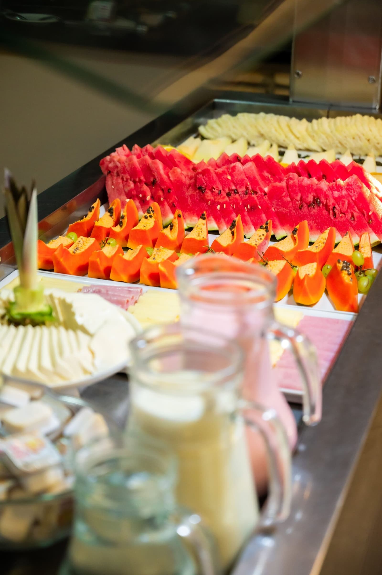 Papaja, watermeloen, kaas, sap, dit buffet maakt geen halve maatregelen voor een volle dag. Een ontbijtbuffet op een Amazon- en Pantanal-tour met rijen gesneden watermeloen en papaja op een roestvrijstalen toonbank, samen met kaas, druiven en glazen karaffen met sap