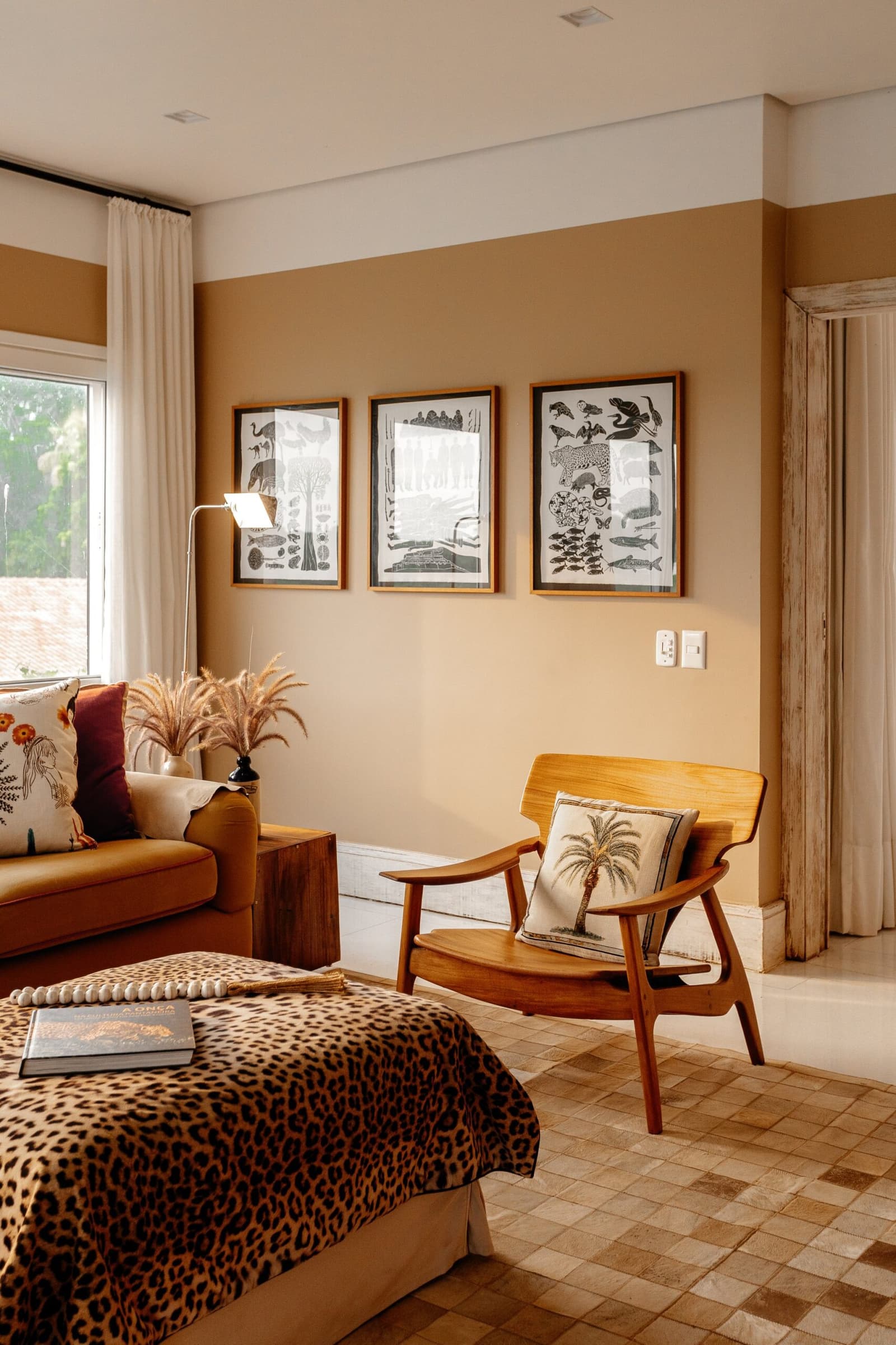 Die Wildnis macht keinen Halt vor der Zimmertür, und das ist gut so. Photo: Felipe Castellari Lodge-Suite-Interieur einer Luxury Pantanal and Amazon Trip mit Leopardenmuster-Tagesdecke, einem Holzsessel im Mid-Century-Stil mit Palmen-Kissen, drei gerahmten Tierillustrations-Drucken an einer warmen Ockerwand und einem Kuhfell-gemusterten Fliesenboden