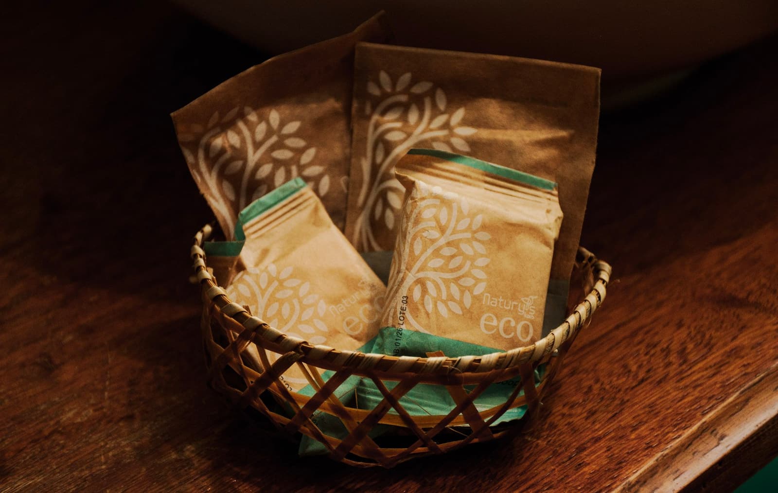 Geen plastic in zicht. Goed voor het geweten, goed voor het woud. Vier kraftpapieren Natury Eco toiletry-zakjes met bladmotief in een geweven mandje op een houten tafelblad, milieuvriendelijke logeerfaciliteiten op een Amazon en Pantanal tour
