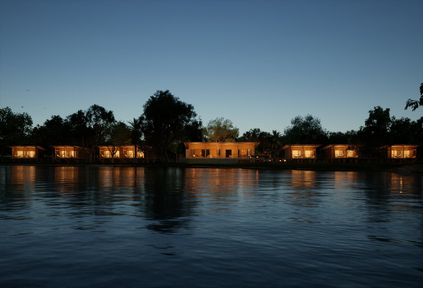 Wenn die Nacht kommt, leuchtet die Lodge, als hätte sie auf Sie gewartet. Eine Reihe warm beleuchteter Öko-Lodge-Bungalows und ein zentraler Pavillon spiegeln sich in der Abenddämmerung auf einem ruhigen Fluss wider – Teil einer Luxusreise durch Pantanal und Amazonas