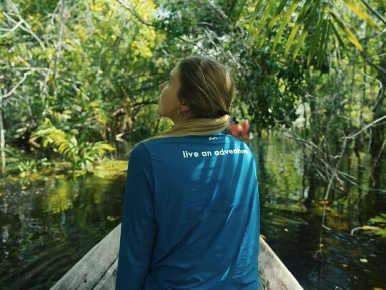 Viajante em uma canoa de madeira observando o dossel da floresta alagada em uma aventura na Amazônia