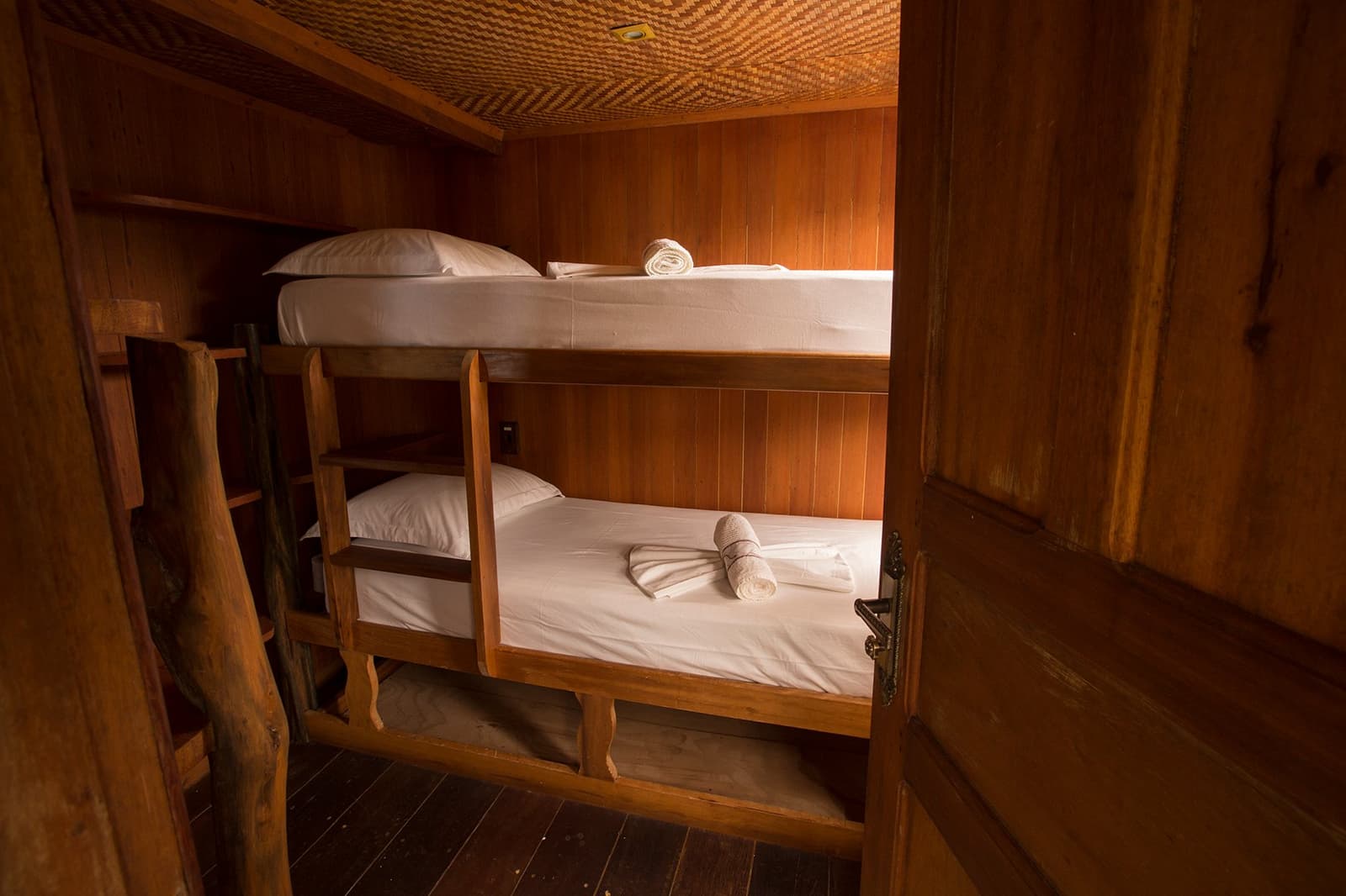 Aconchegante, arrumada, e com a floresta esperando logo ali fora. Cabine de madeira com beliche em um cruzeiro pelo Rio Amazonas no Brasil, com roupa de cama branca, toalhas dobradas e uma escada rústica