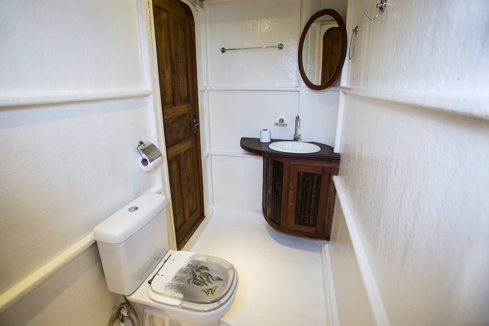 No fundo da floresta, até o banheiro tem personalidade. Banheiro privativo compacto a bordo de um cruzeiro pelo Rio Amazonas no Brasil, com vaso sanitário branco de tampa estampada, bancada de madeira escura com cuba redonda e espelho oval