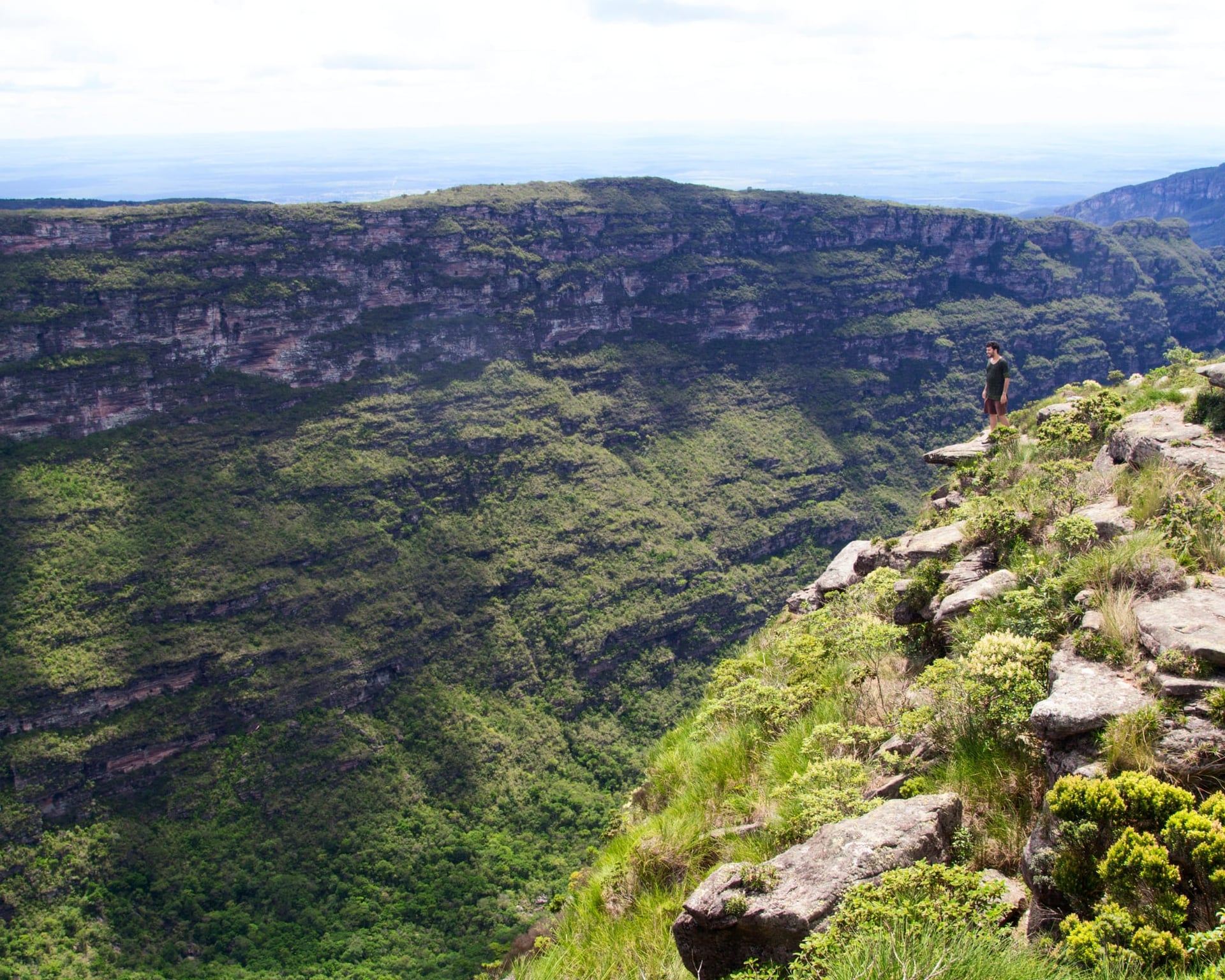 A hiker standing at the edge of a cliff overlooking a green valley in Chapada Diamantina, Brazil. A hiker standing at the edge of a cliff overlooking a green valley in Chapada Diamantina, Brazil.