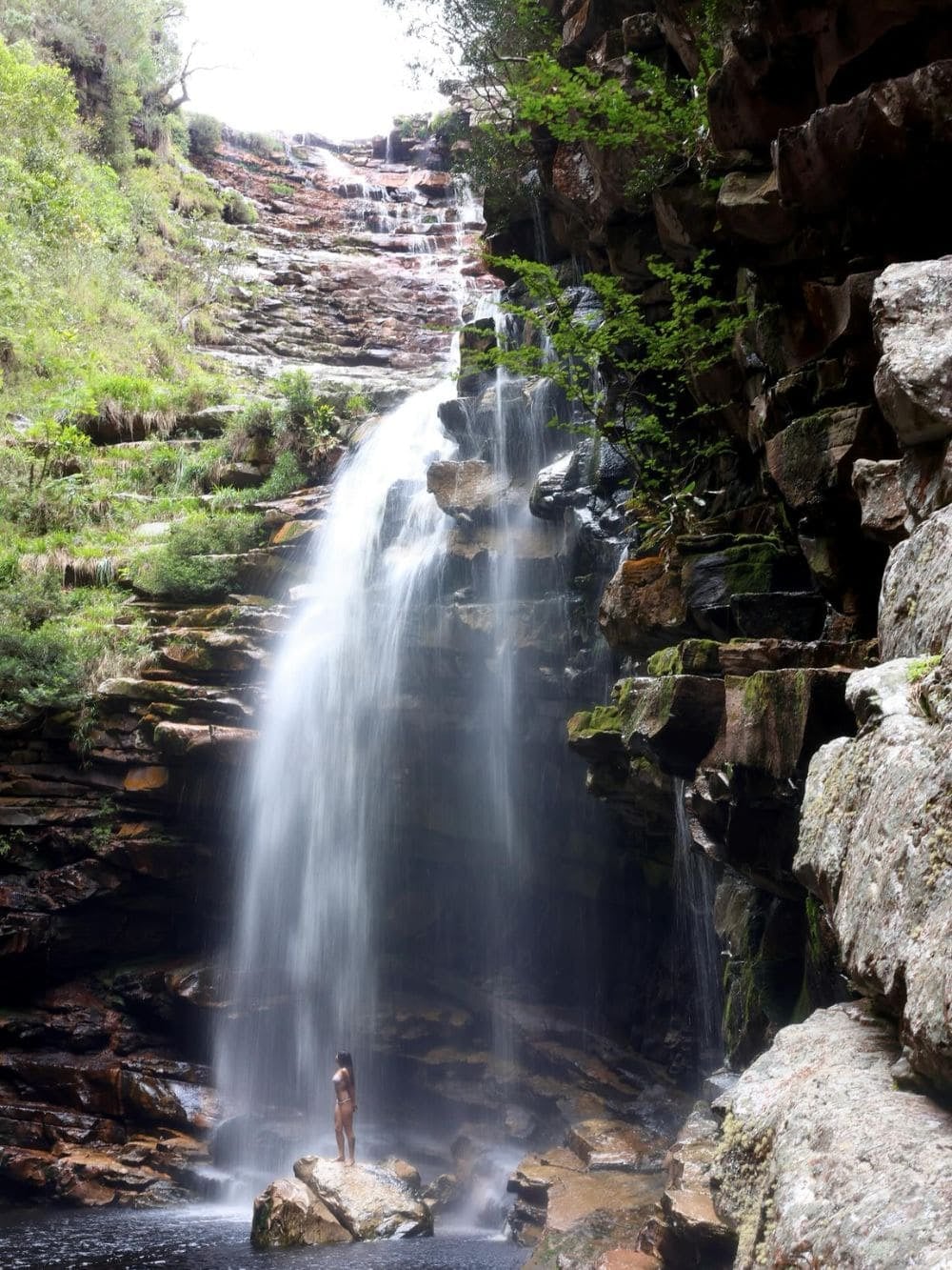 Una persona in piedi su una roccia ai piedi di un'alta cascata nella Vale do Pati, nella Chapada Diamantina, in Brasile. Una persona in piedi su una roccia ai piedi di un'alta cascata nella Vale do Pati, nella Chapada Diamantina, in Brasile.