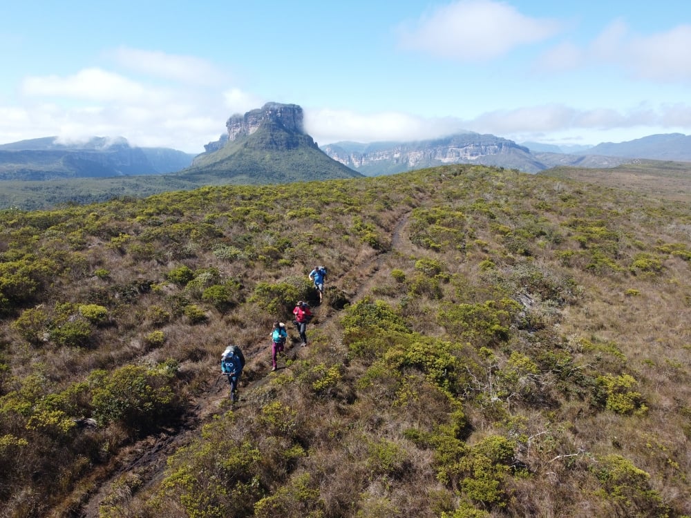Aerial view of hikers crossing a plateau trail toward a flat-topped mountain in Chapada Diamantina, Brazil. Aerial view of hikers crossing a plateau trail toward a flat-topped mountain in Chapada Diamantina, Brazil.