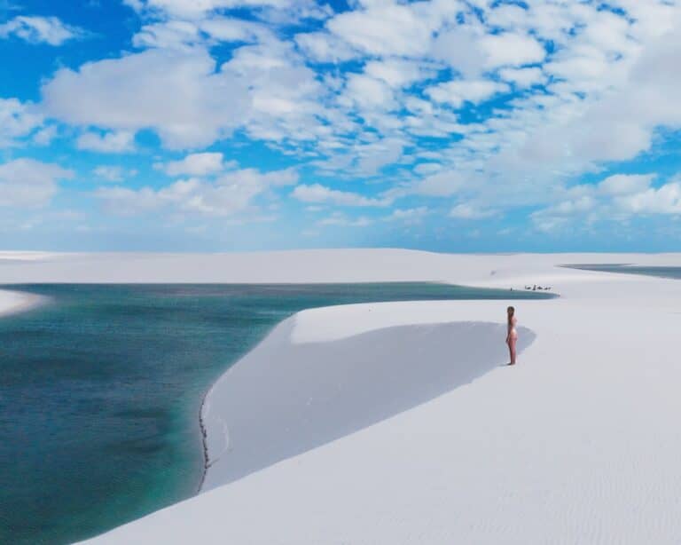Woman standing on a white dune above a turquoise lagoon in Lençóis Maranhenses under a blue sky